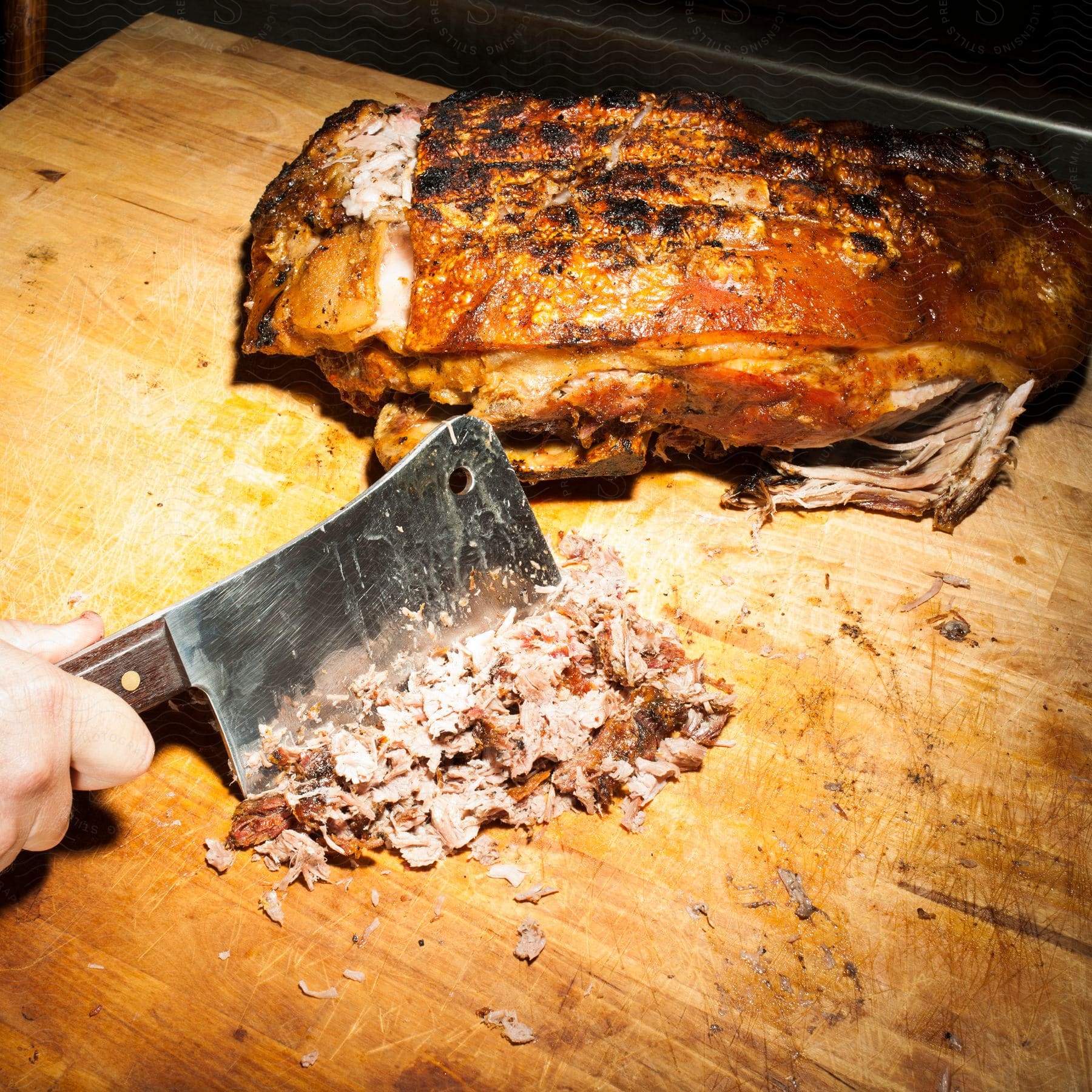 A chef is chopping grilled beef with a knife on a wooden surface