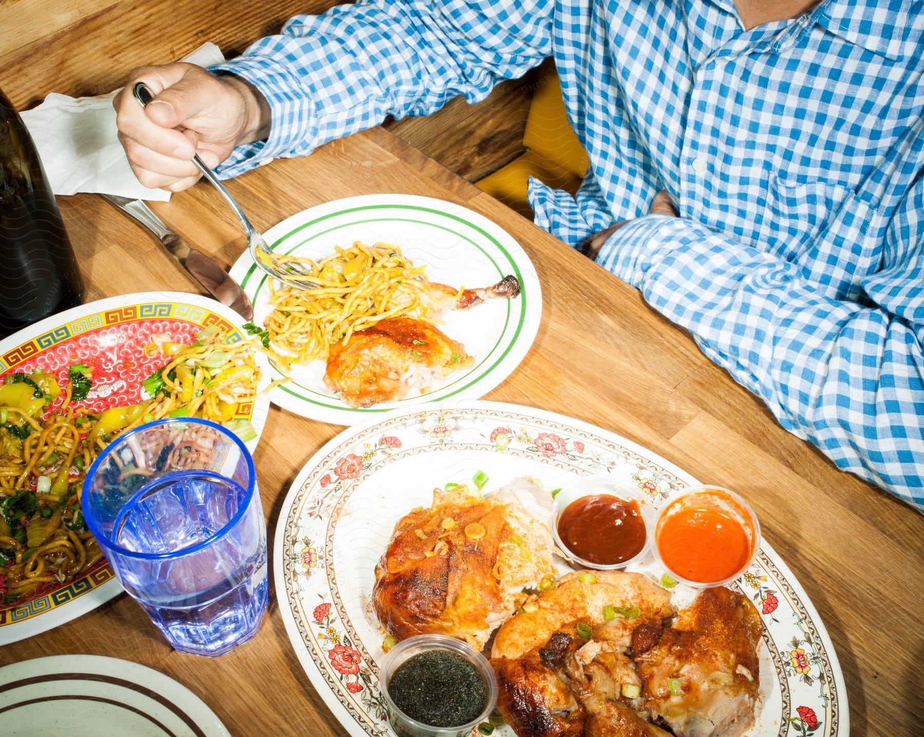 A man is seen having lunch with pasta and fried chicken on a wooden table