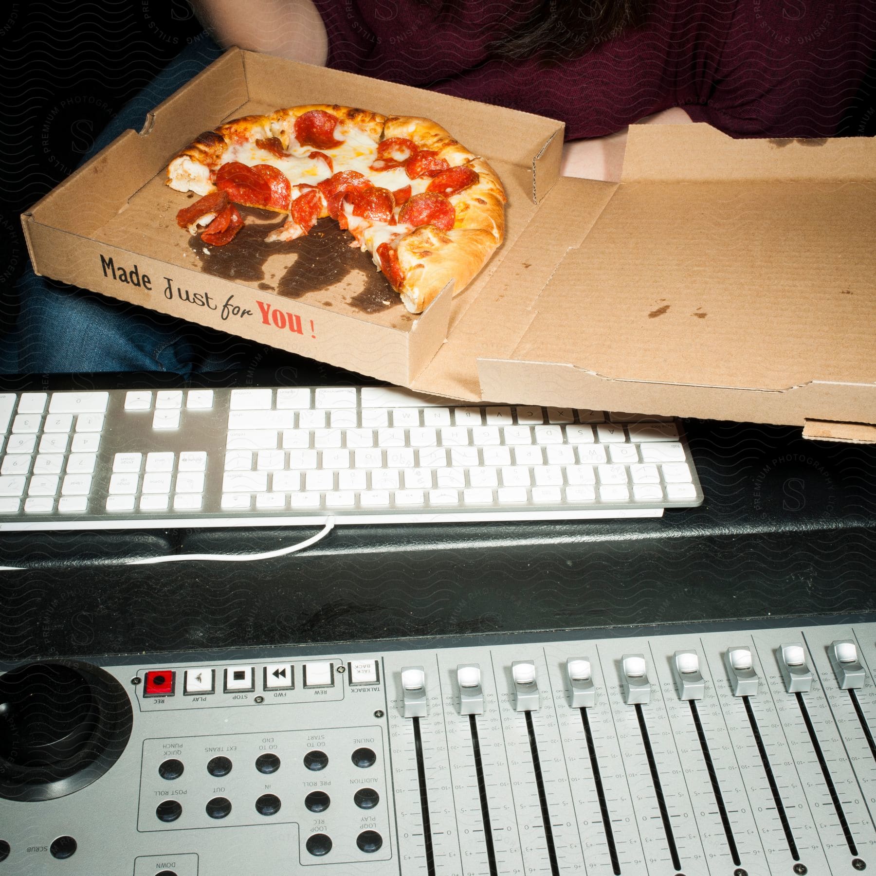 A woman in a red shirt and jeans holds a halfeaten pizza near her computer keyboard