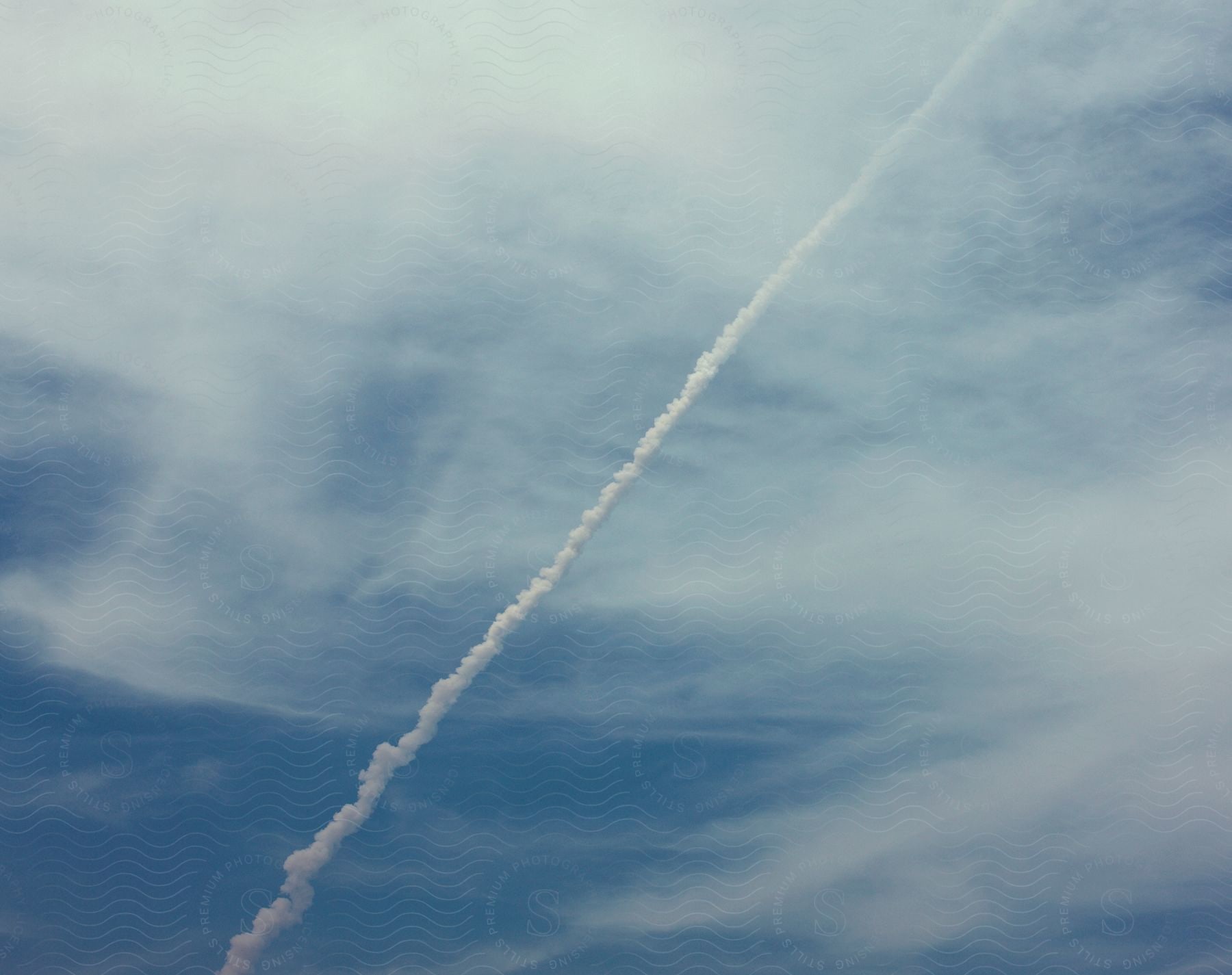 Rocket taking off with a trail against a blue cloudy sky