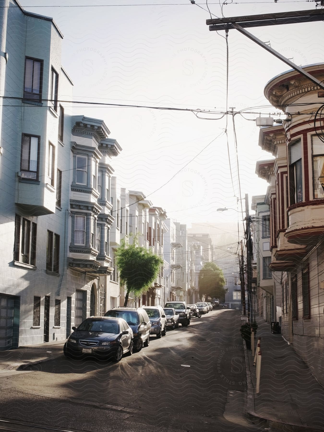 Cars parked on the street in front of apartment buildings as the sun shines in a hazy sky