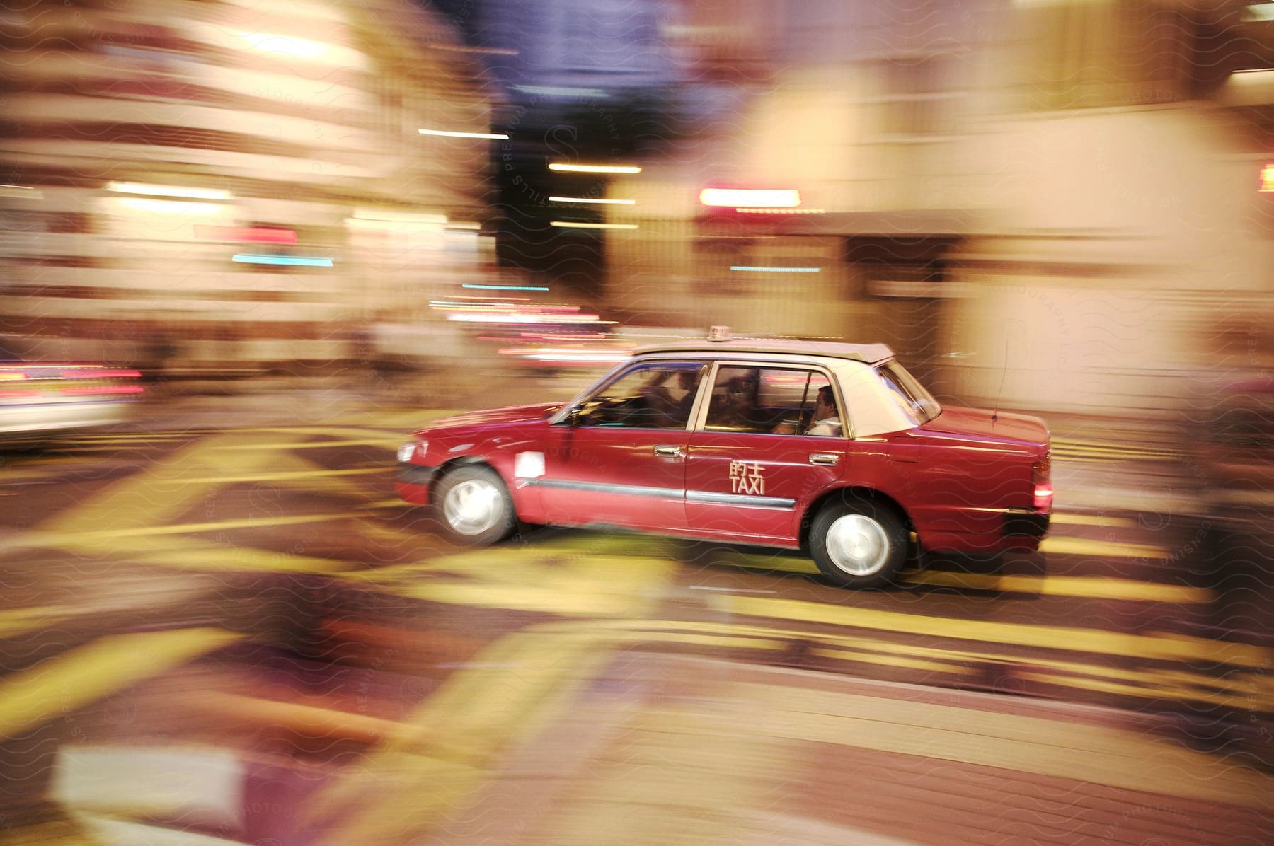 A red hong kong style taxi car is still in the middle of a moving blurred city street at night