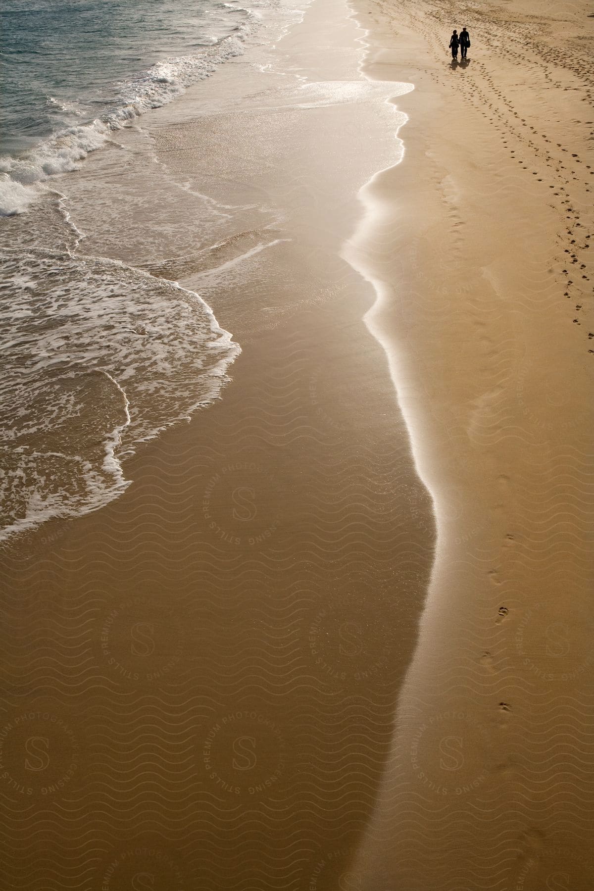 Two people walk on a sand beach close to the water on a sunny day