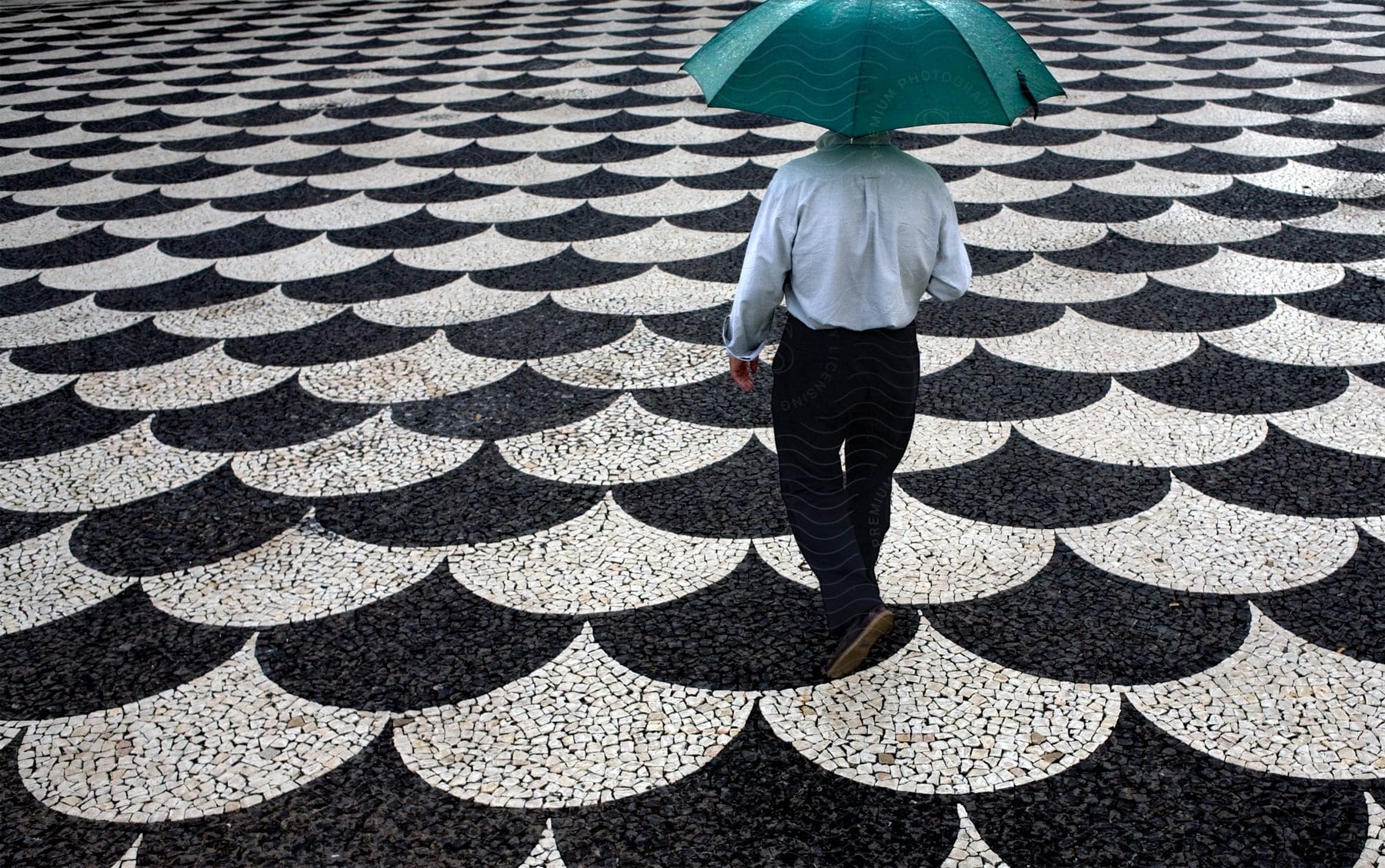 A man without a jacket holds a turquoise umbrella on a patterned floor