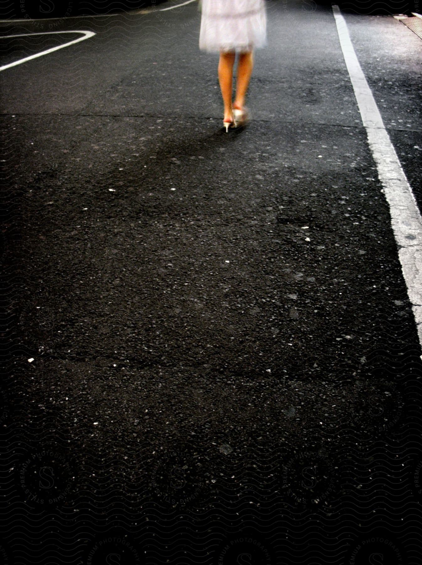 A woman wearing a white dress and high heels walks on an asphalt road