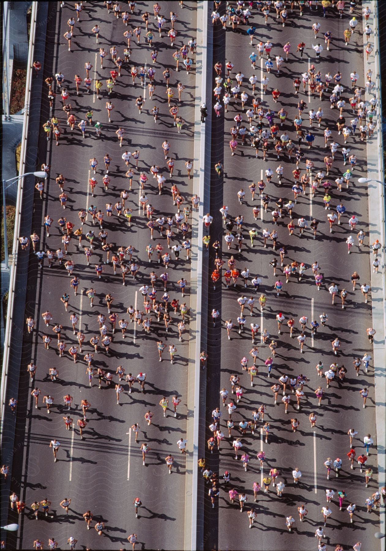 A large group of competitive runners race across a multiple lane highway through a city