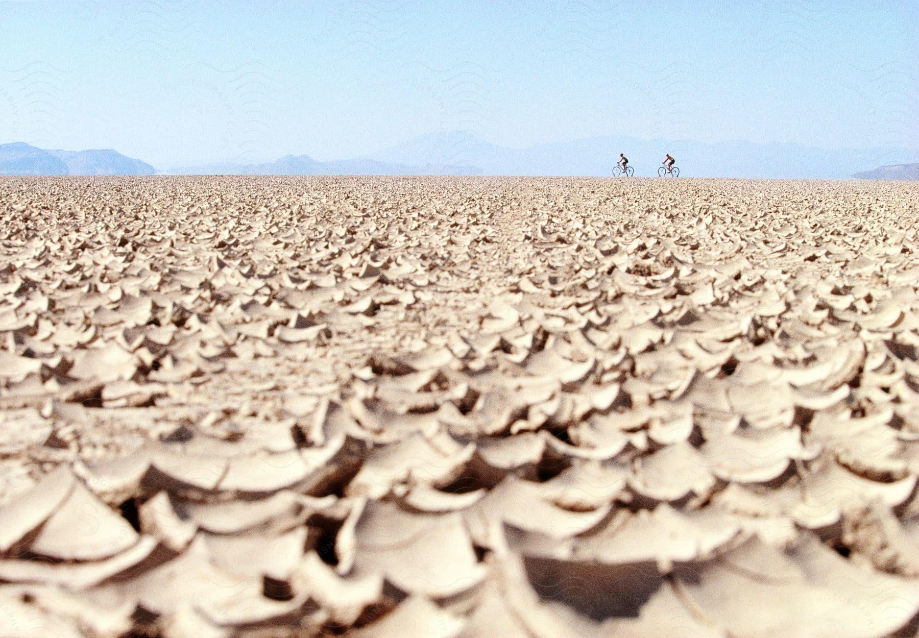 Two cyclists ride over the dry desert soil on the horizon