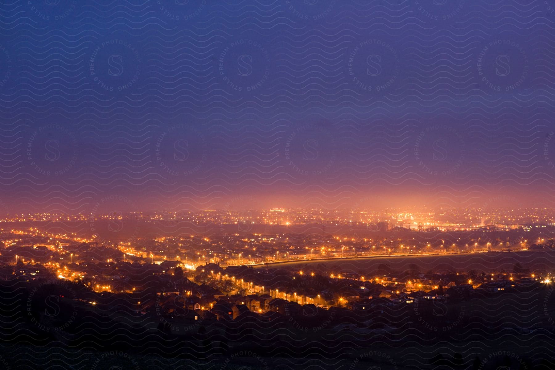 Orange lights of cityscape tint fog under dark blue night sky