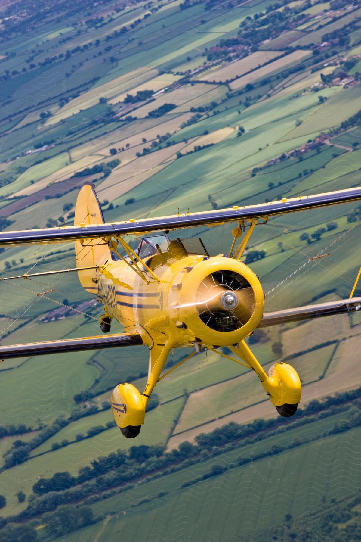 A propeller plane is being flown by two pilots over farmland