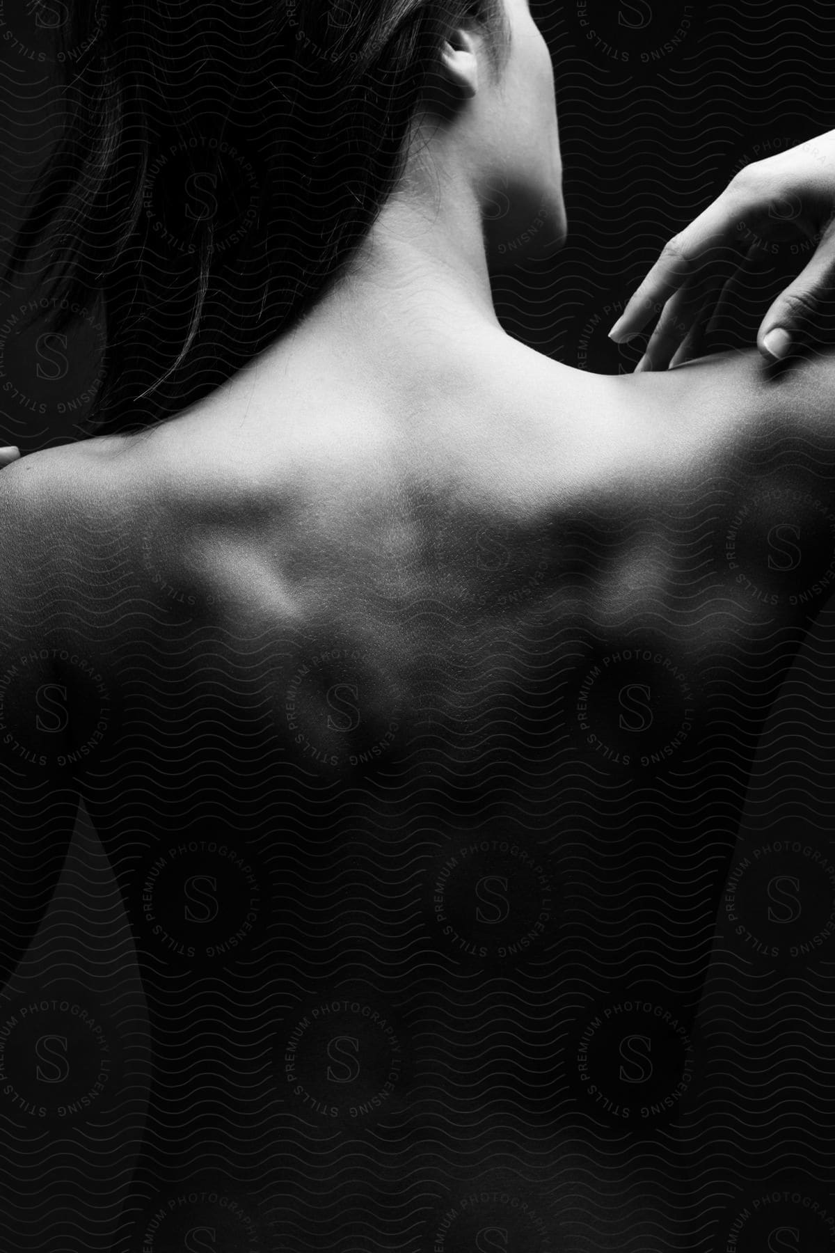 A black and white image of a womans bare back as she touches her shoulder