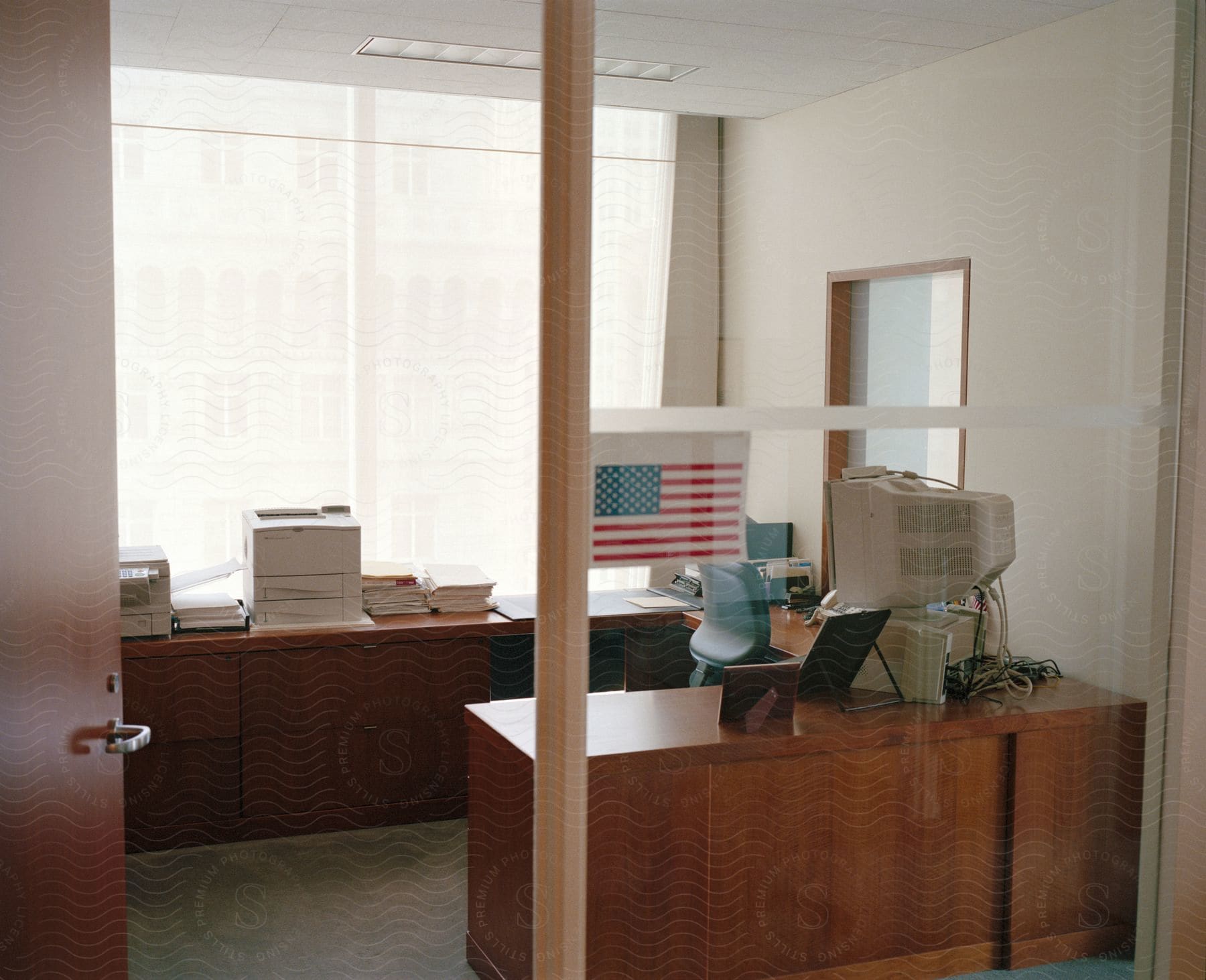 An office building with an american flag in the window a computer on the desk and a printer as well
