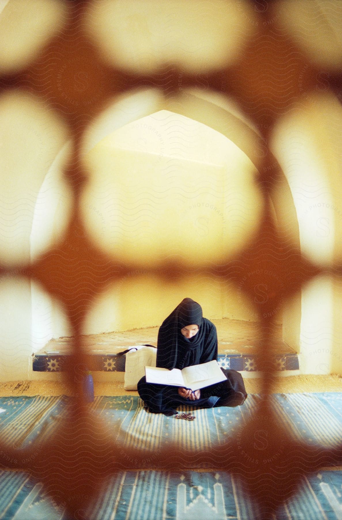 A muslim woman sitting on the floor is reading from a book