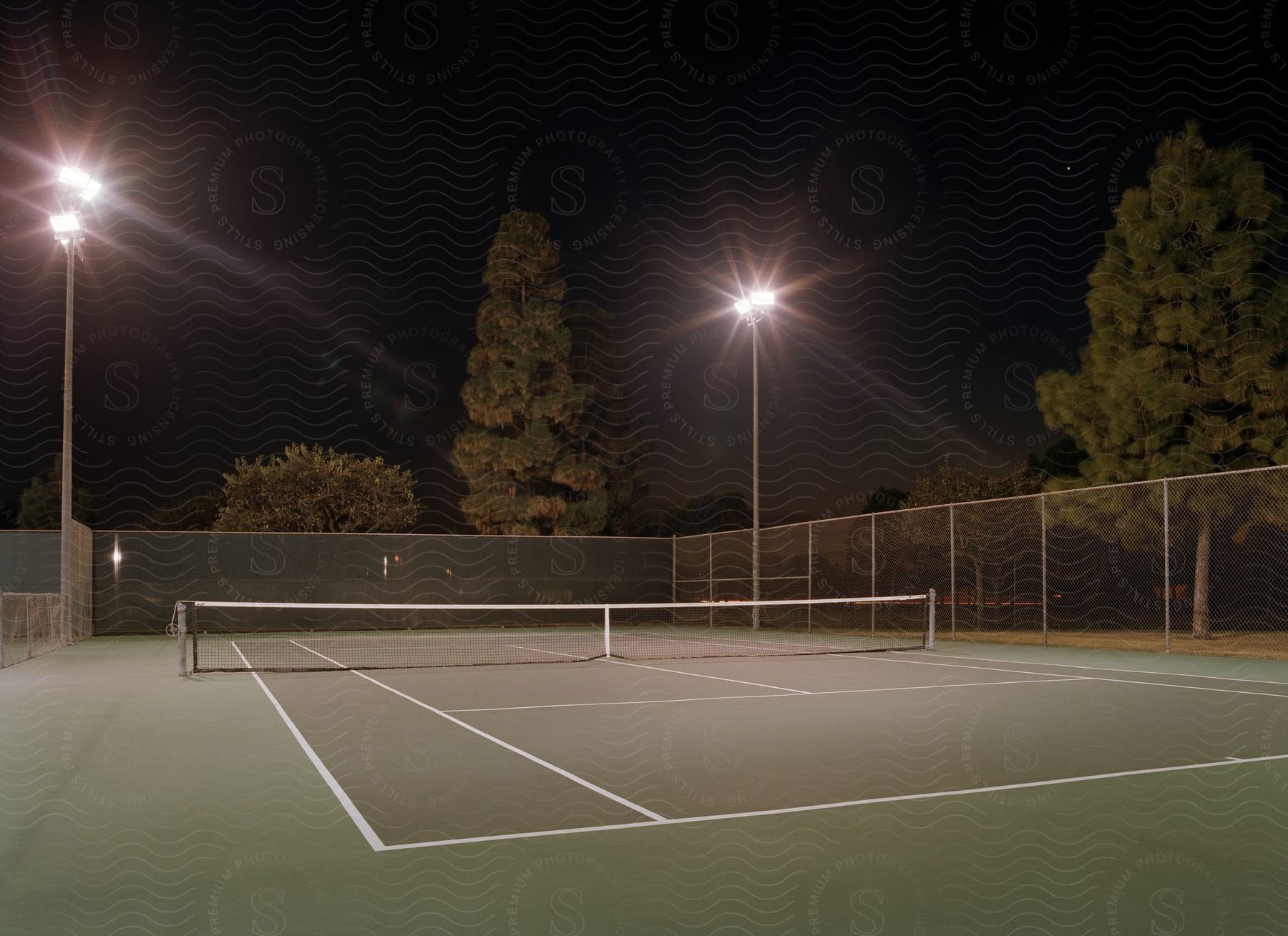Exterior view of a tennis court at night with floodlights illuminating the empty court