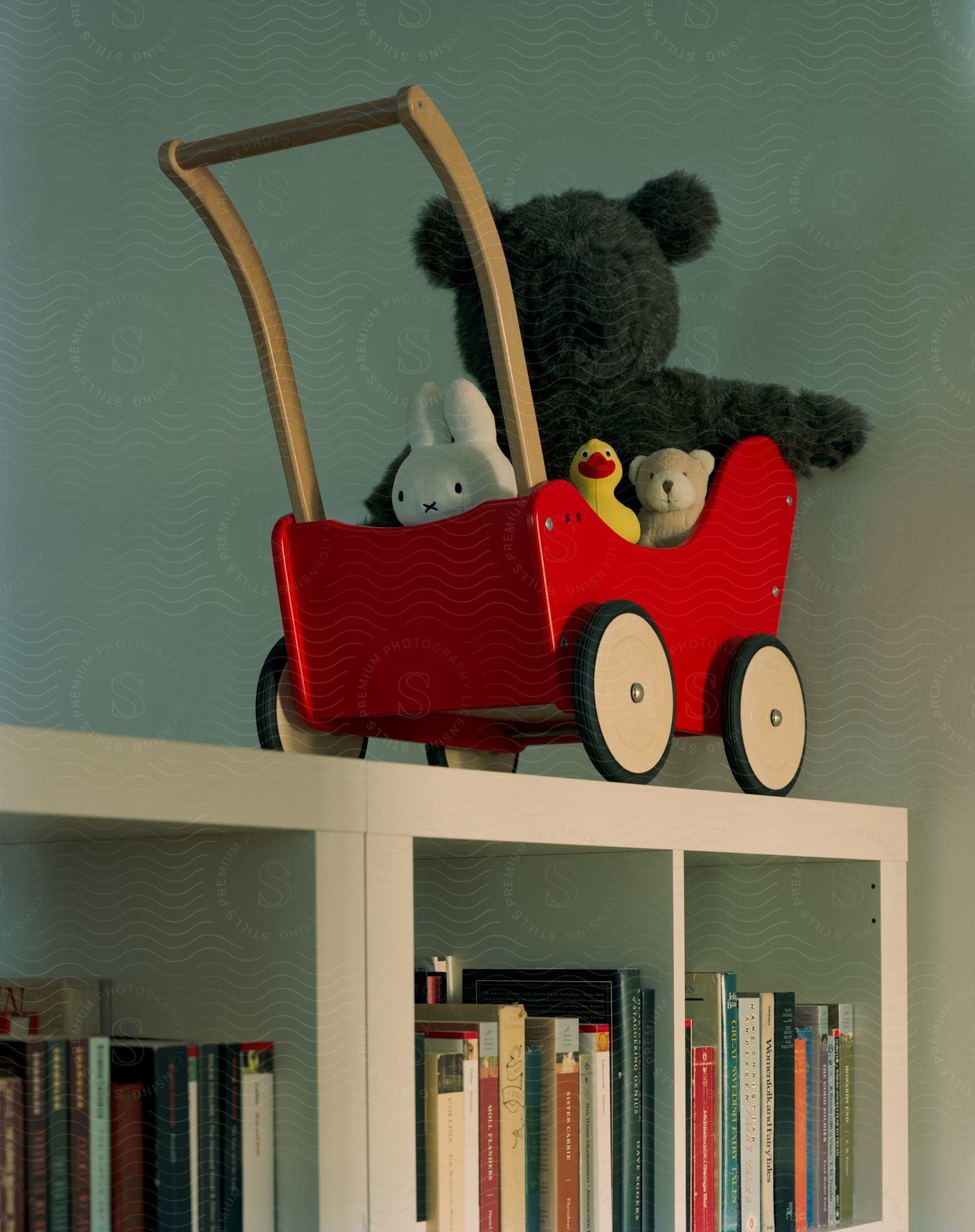 Stuffed toys in red toy wagon sit on white bookcase