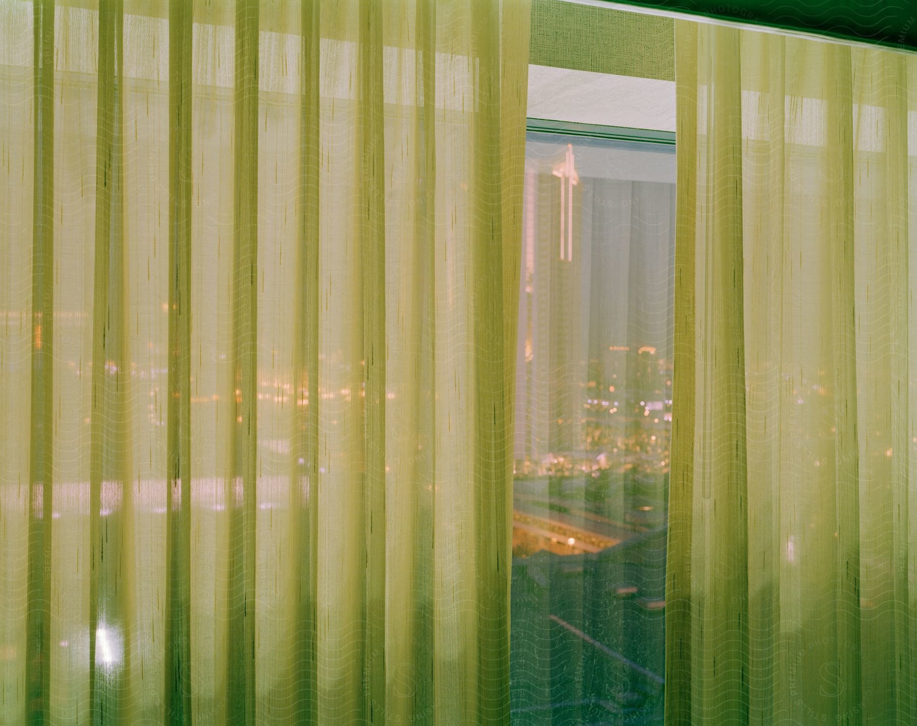 A cityscape seen through a sheer curtaincovered hotel room window