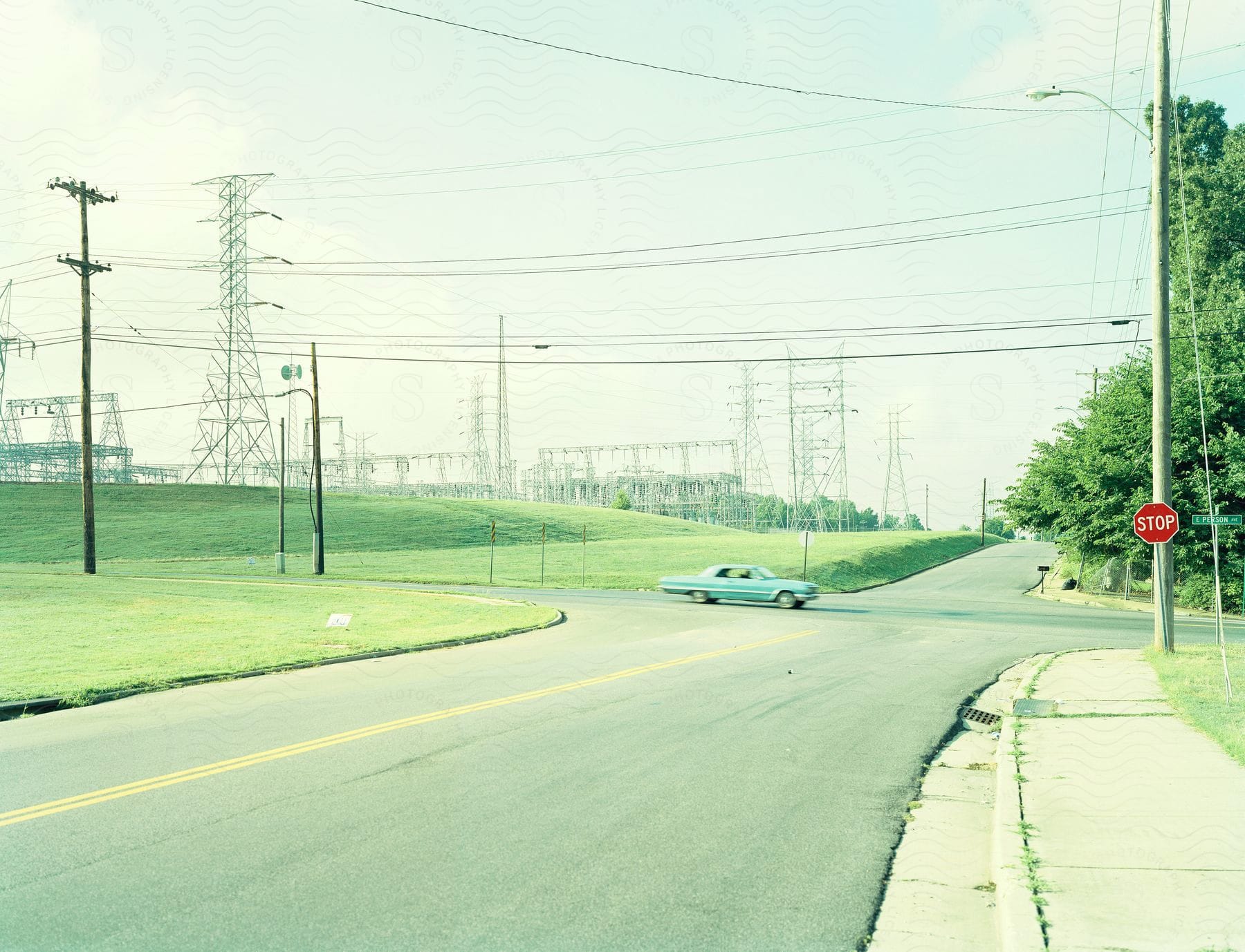 Mint green car at country intersection near grass fields and power station with powerlines