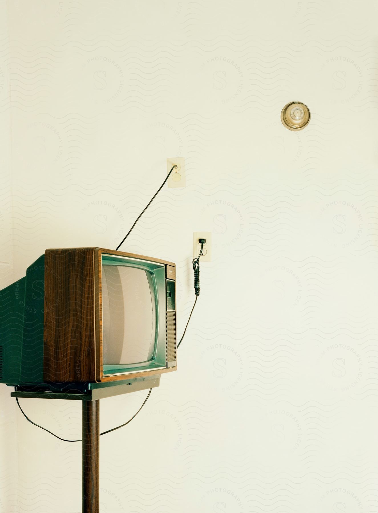 An old wood box frame antenna tv on a metal tv stand plugged into a white wall with an old round thermostat