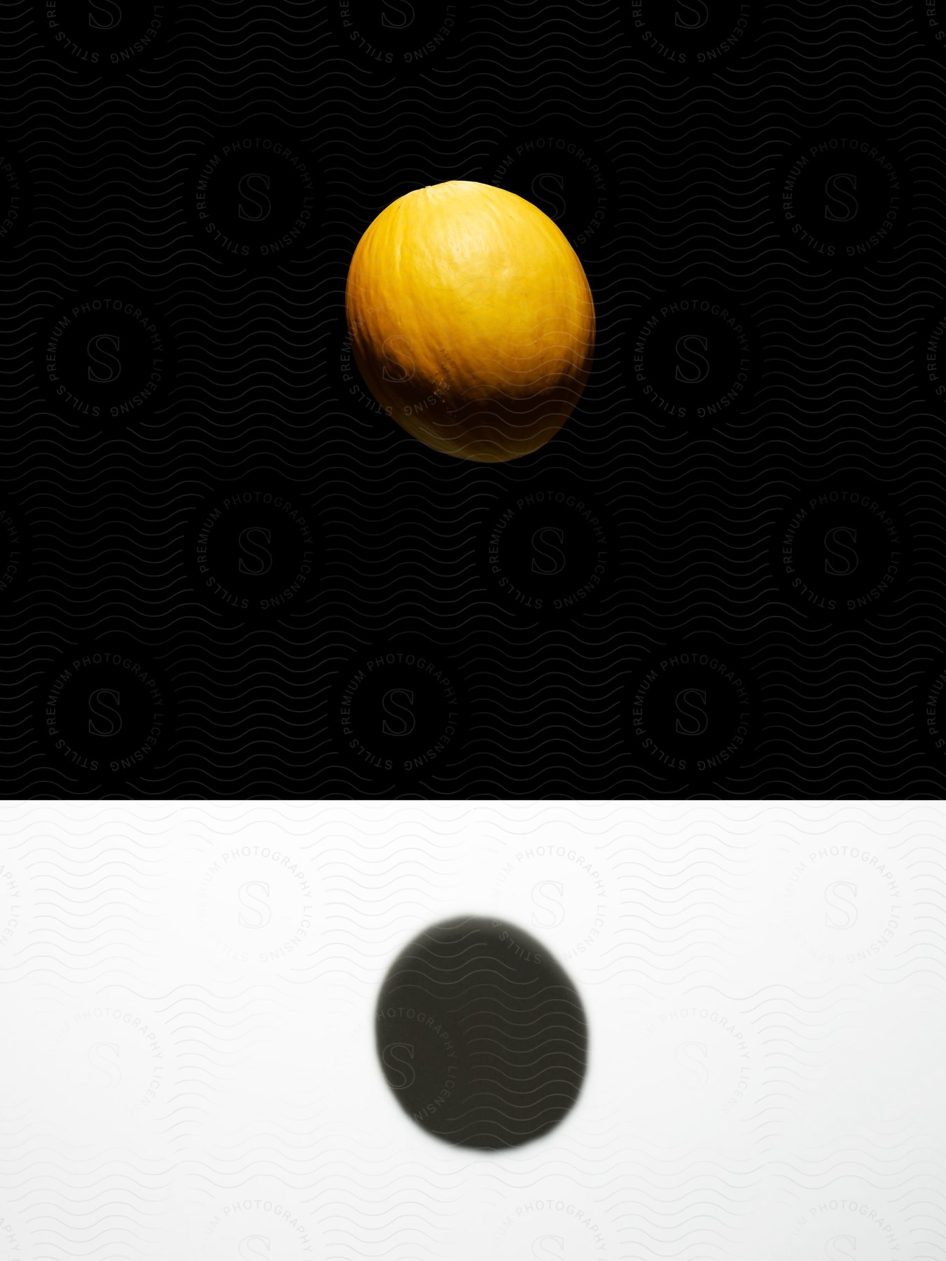 A spherical fruit is floating in the air casting a shadow on a white ground