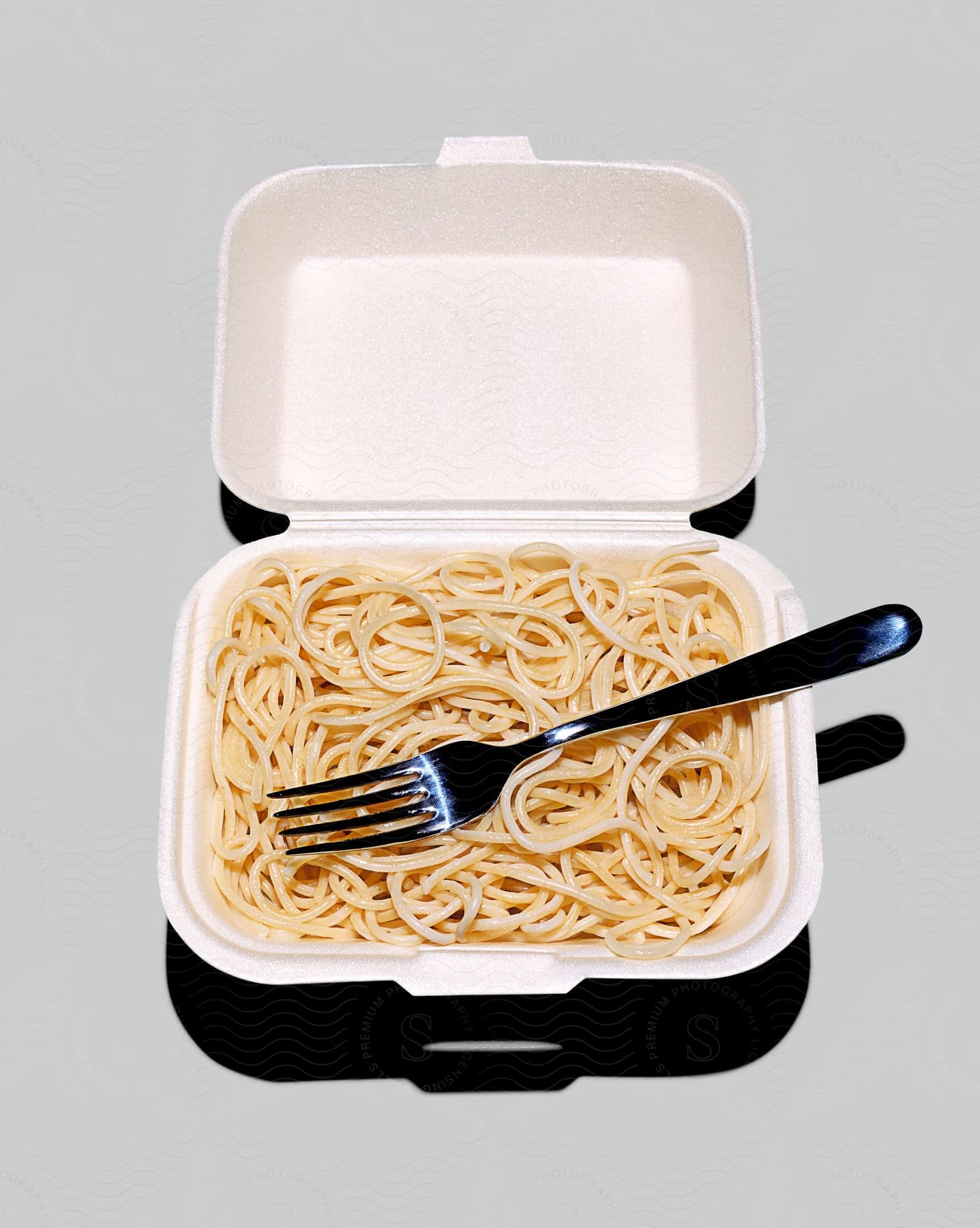 A take out box of pasta with a fork in it on a grey background