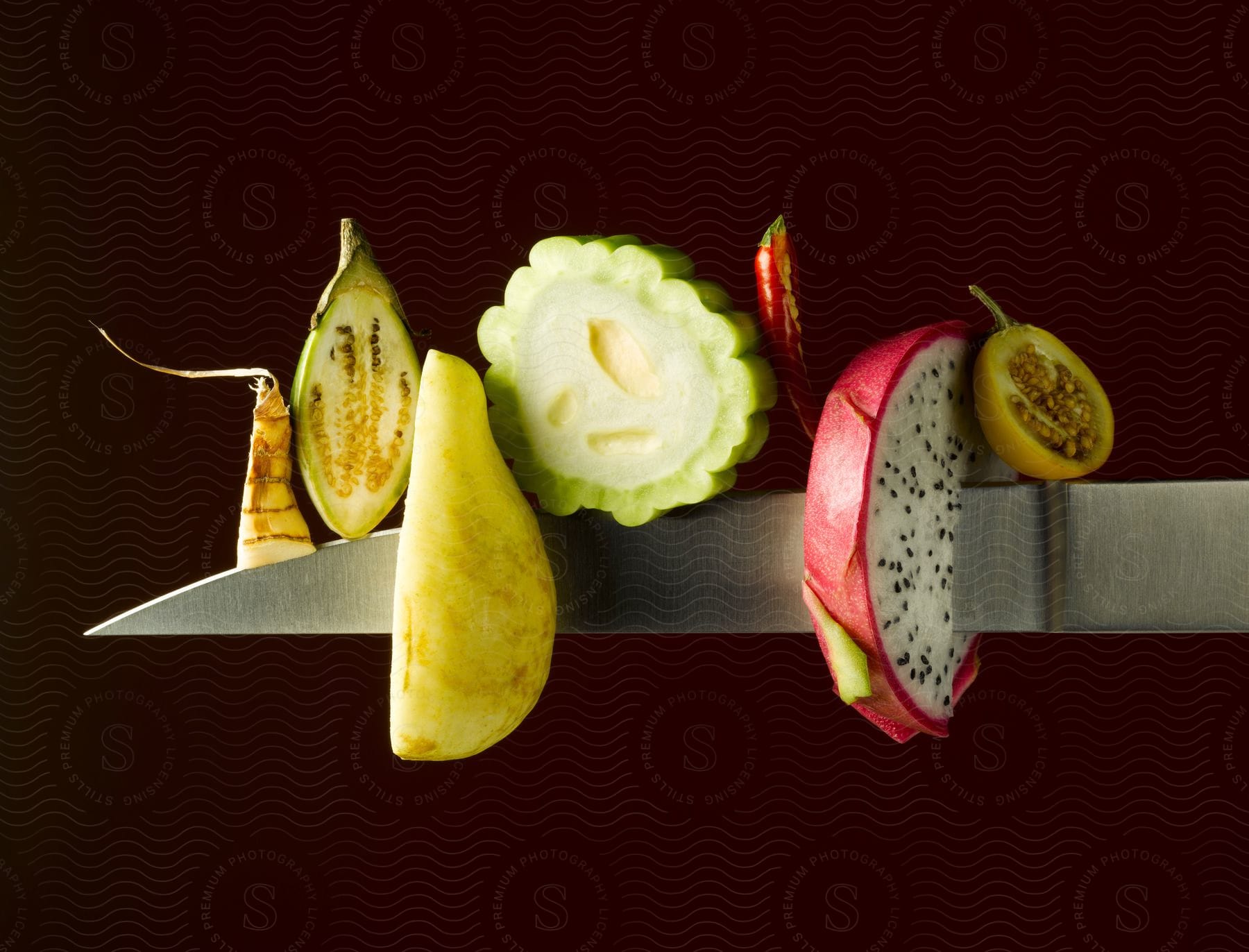 A pear and a slice of dragon fruit pierced by a knife with corn and other fruits on the knifes edge