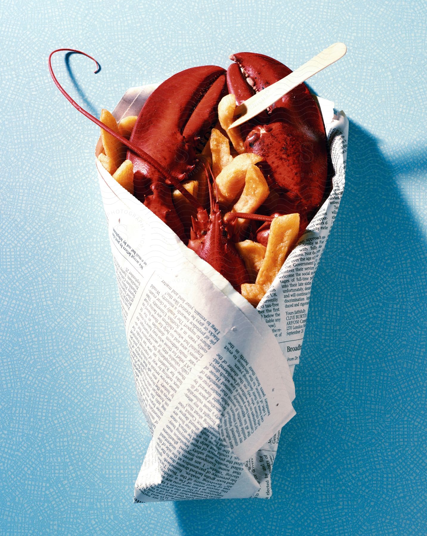 A newspaper wrapped around a freshly cooked lobster and fries all sitting on a blue table top