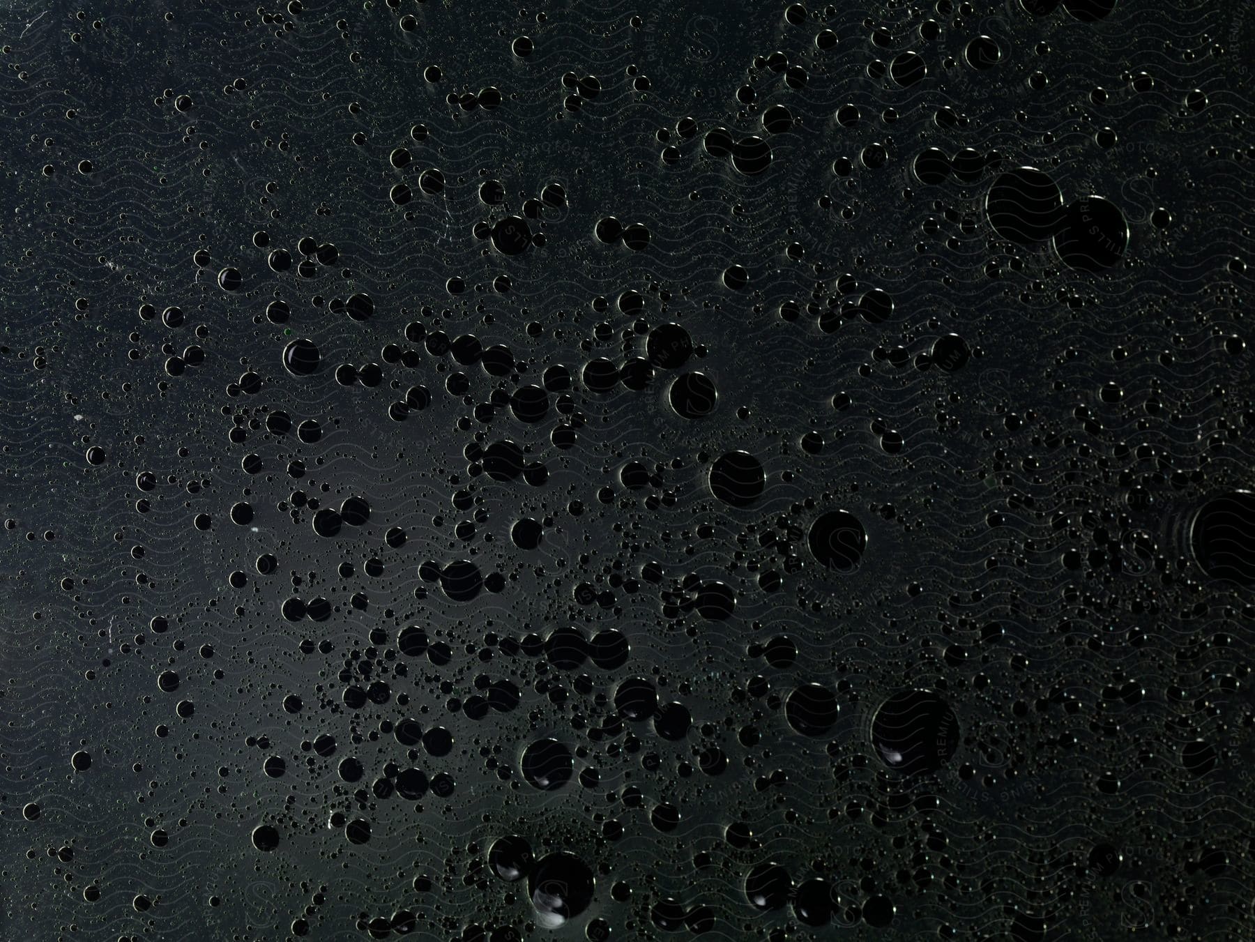 Hundreds of black liquid droplets against a black background