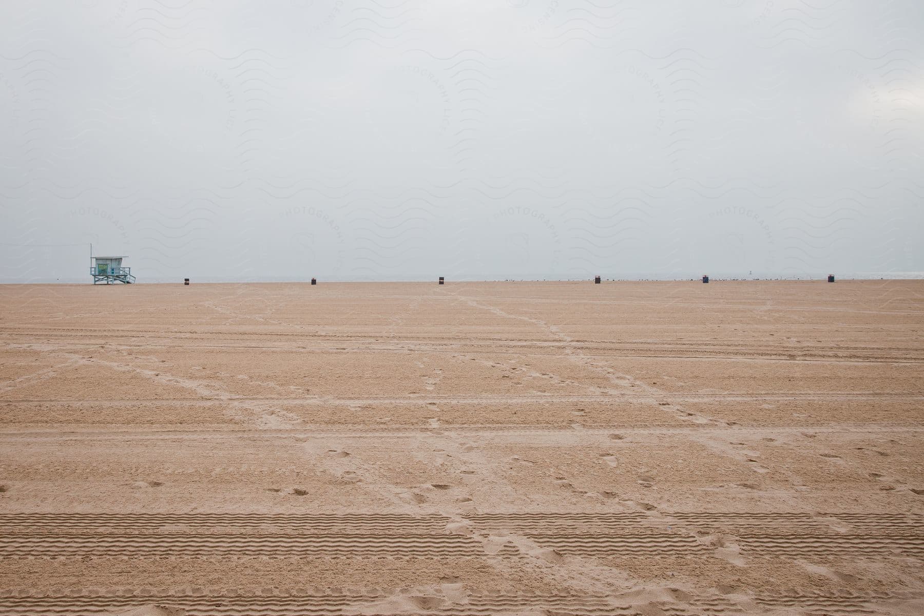 Footprints on sandy beach with lifeguard stand and trash cans in row on cloudy day