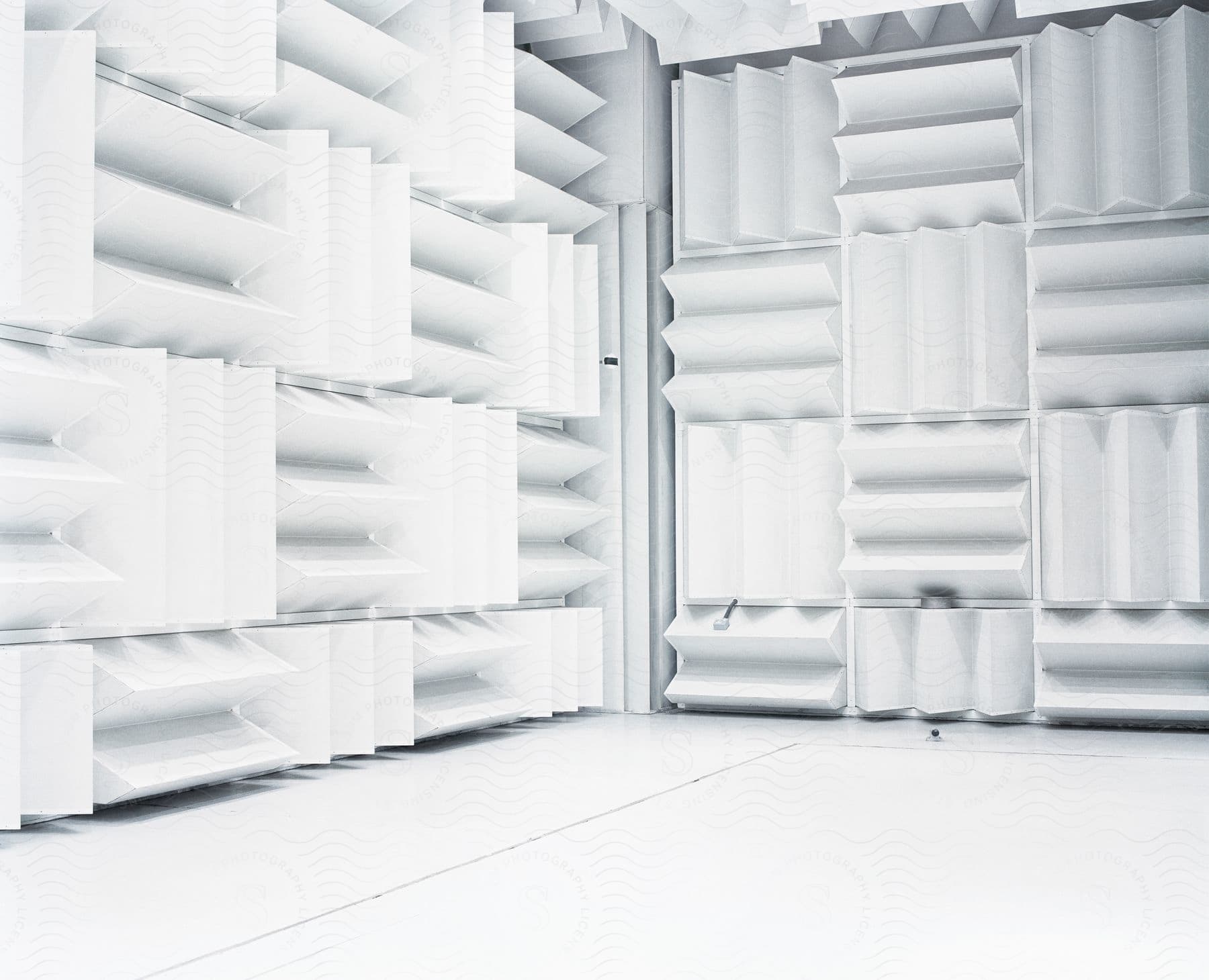 A room with white flooring and acoustic rippled foam padded walls under a bright light