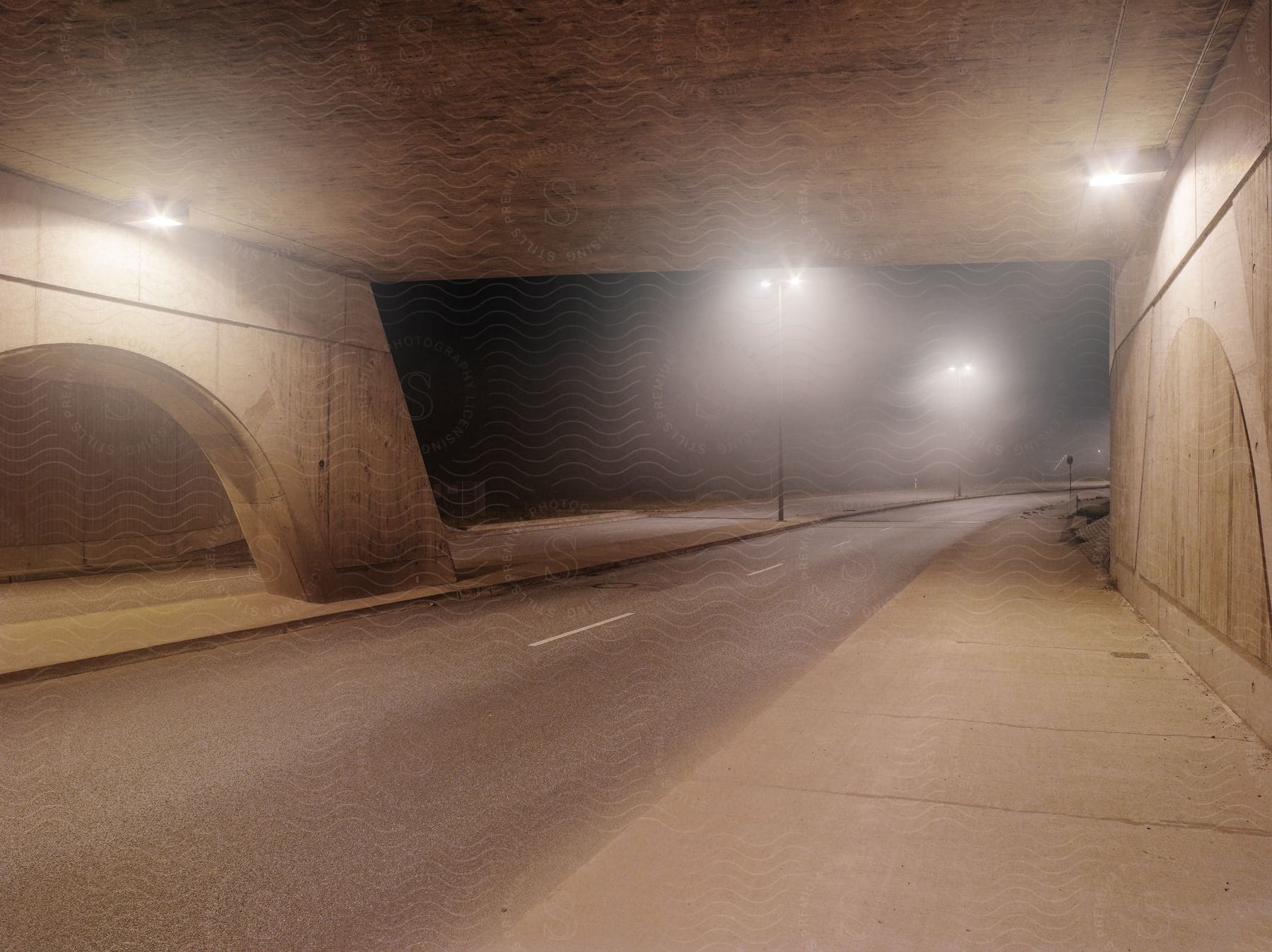 Street under a cement bridge with blurred city street lights covered by a thin fog at night