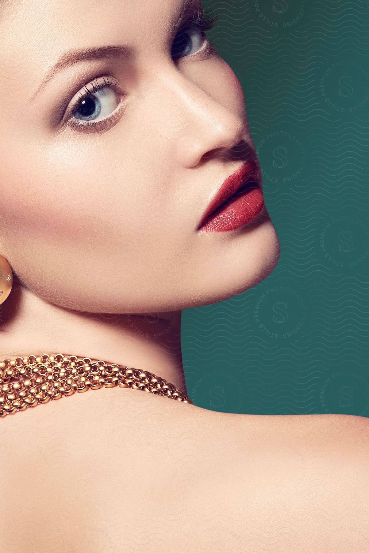 A female with a large gold necklace and red lipstick posing from the shoulders up