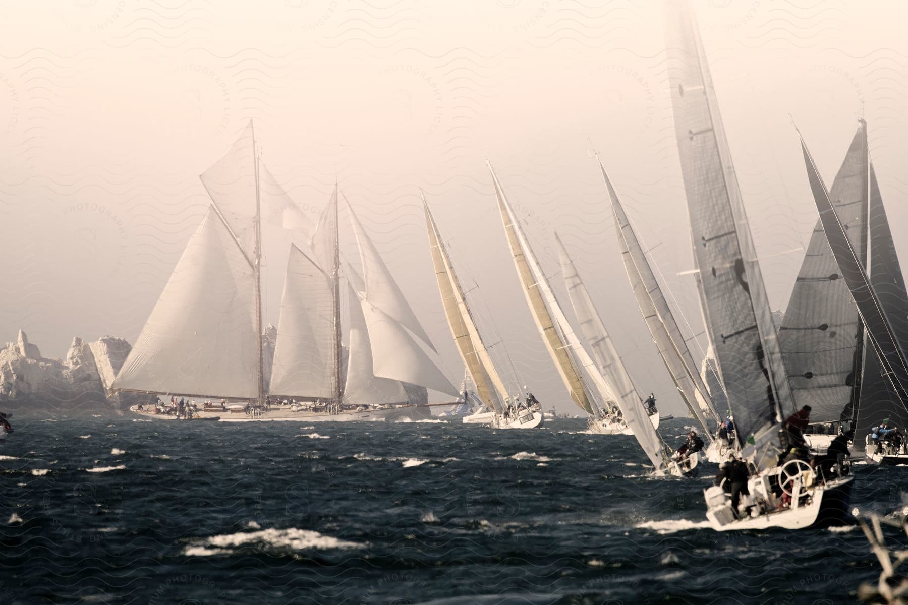 A group of sailing teams compete in a foggy ocean race their sails billowing in the wind