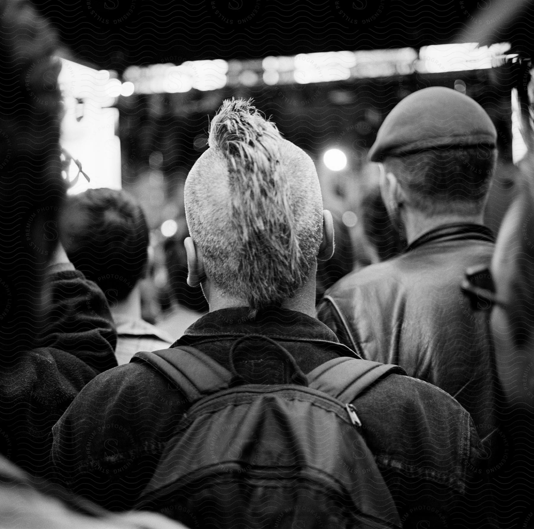 Several Men Seen From Behind Are Gathered In A Crowd At A Music Festival Near Times Square Nyc Listening To The Famous Pop Electronic Band Devo