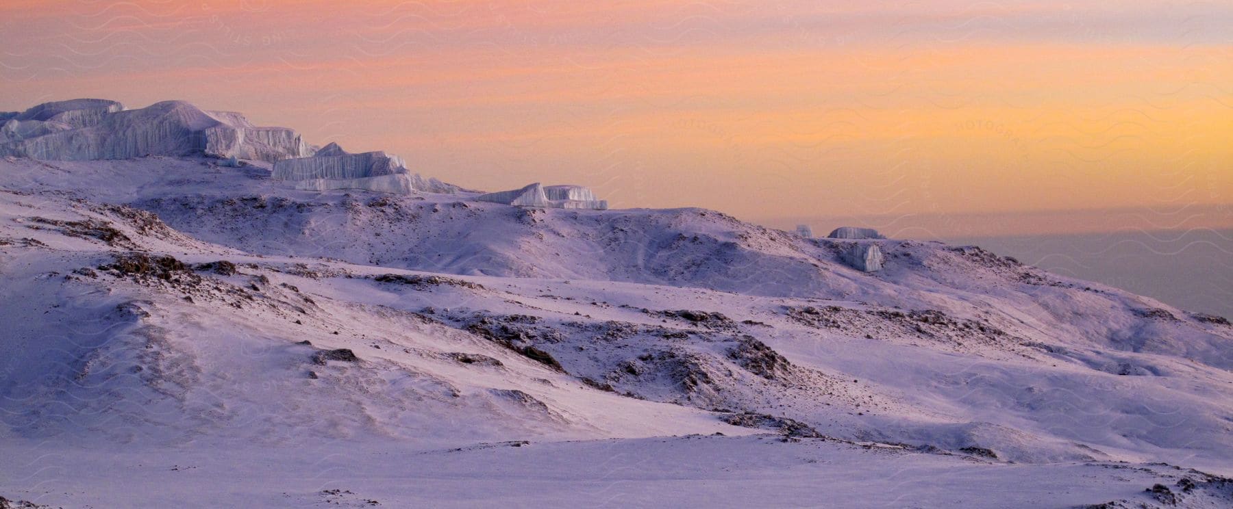 A snowcovered mountain stands along the coast under an orange sunset sky