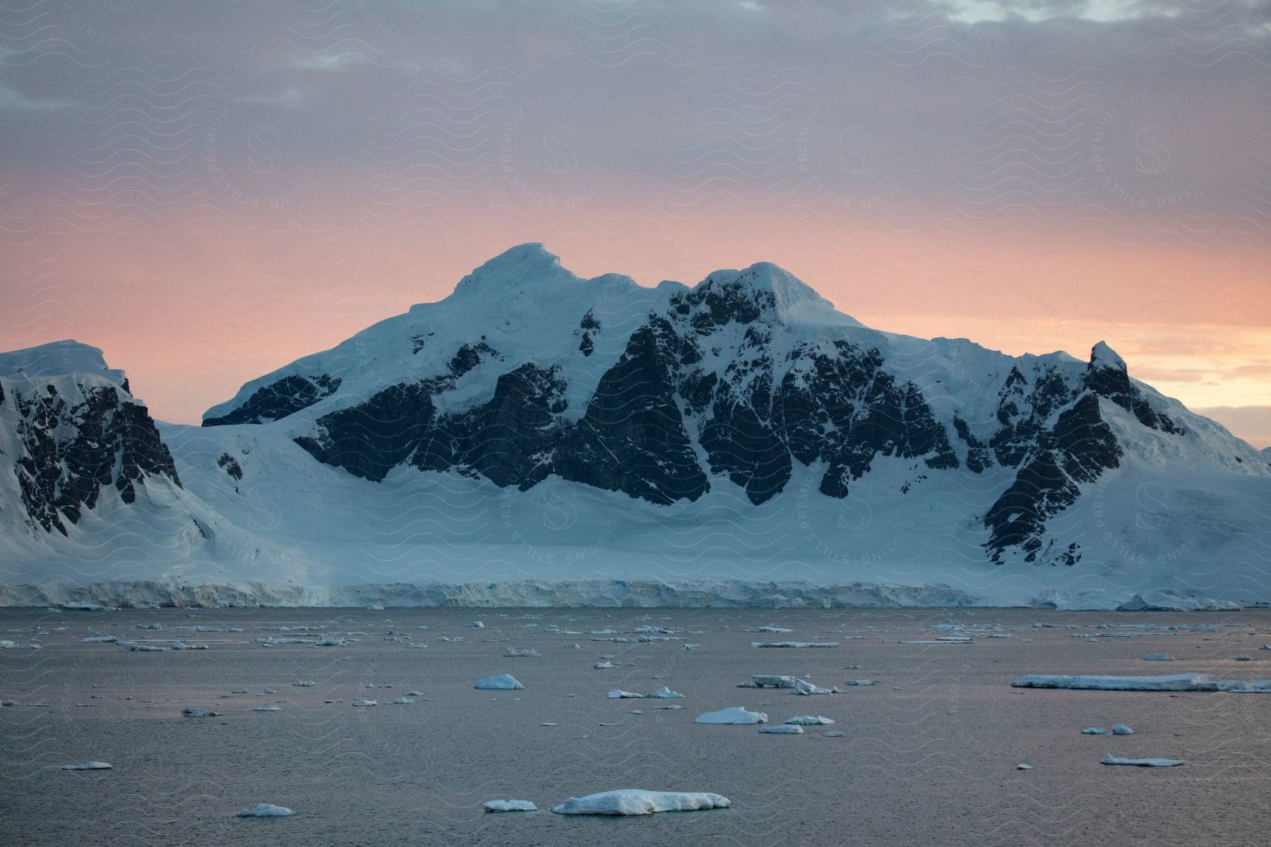 A snowcapped arctic mountain at sunset with ice floes in the water