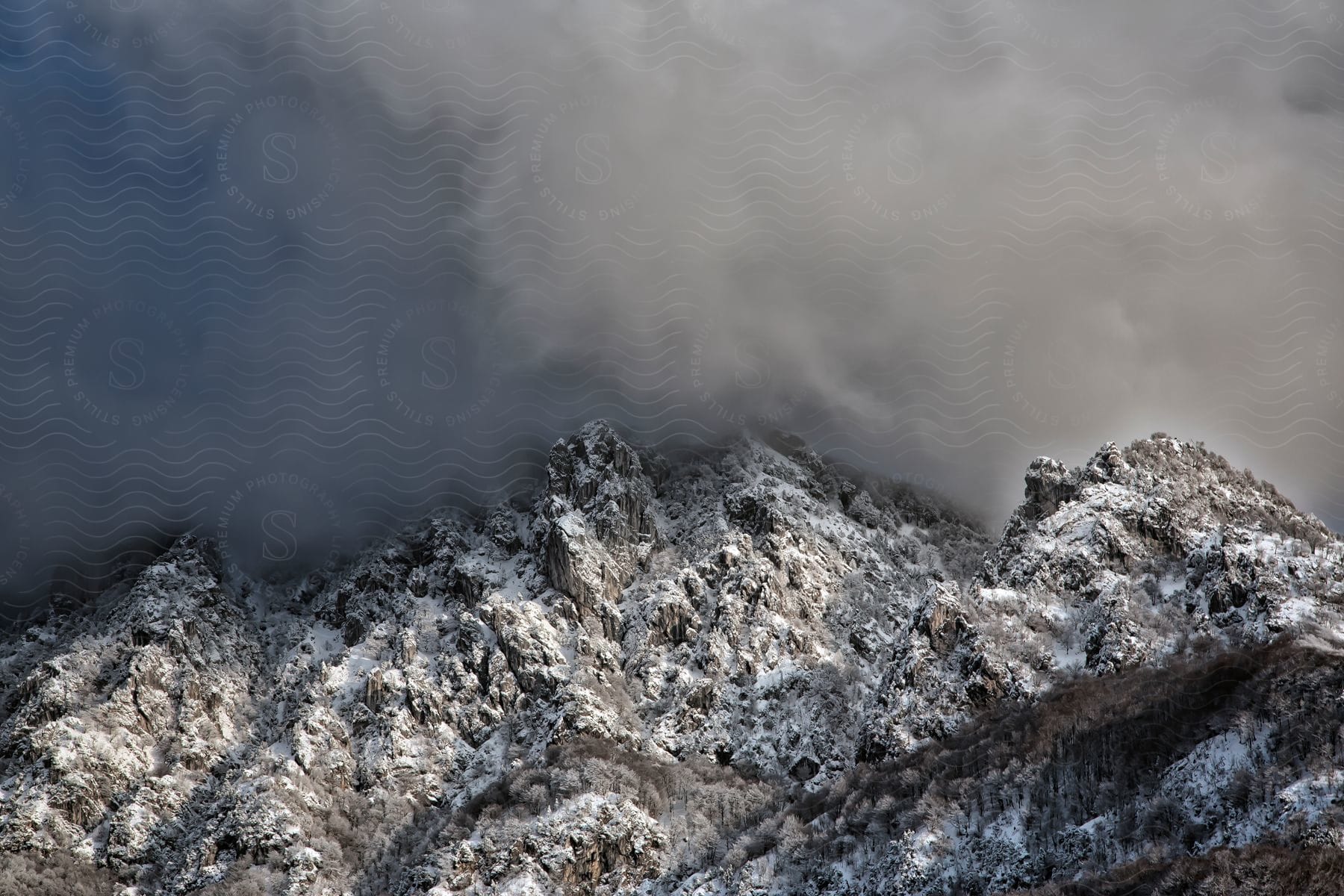 Rocky snowcovered mountain peaks enveloped by grey clouds