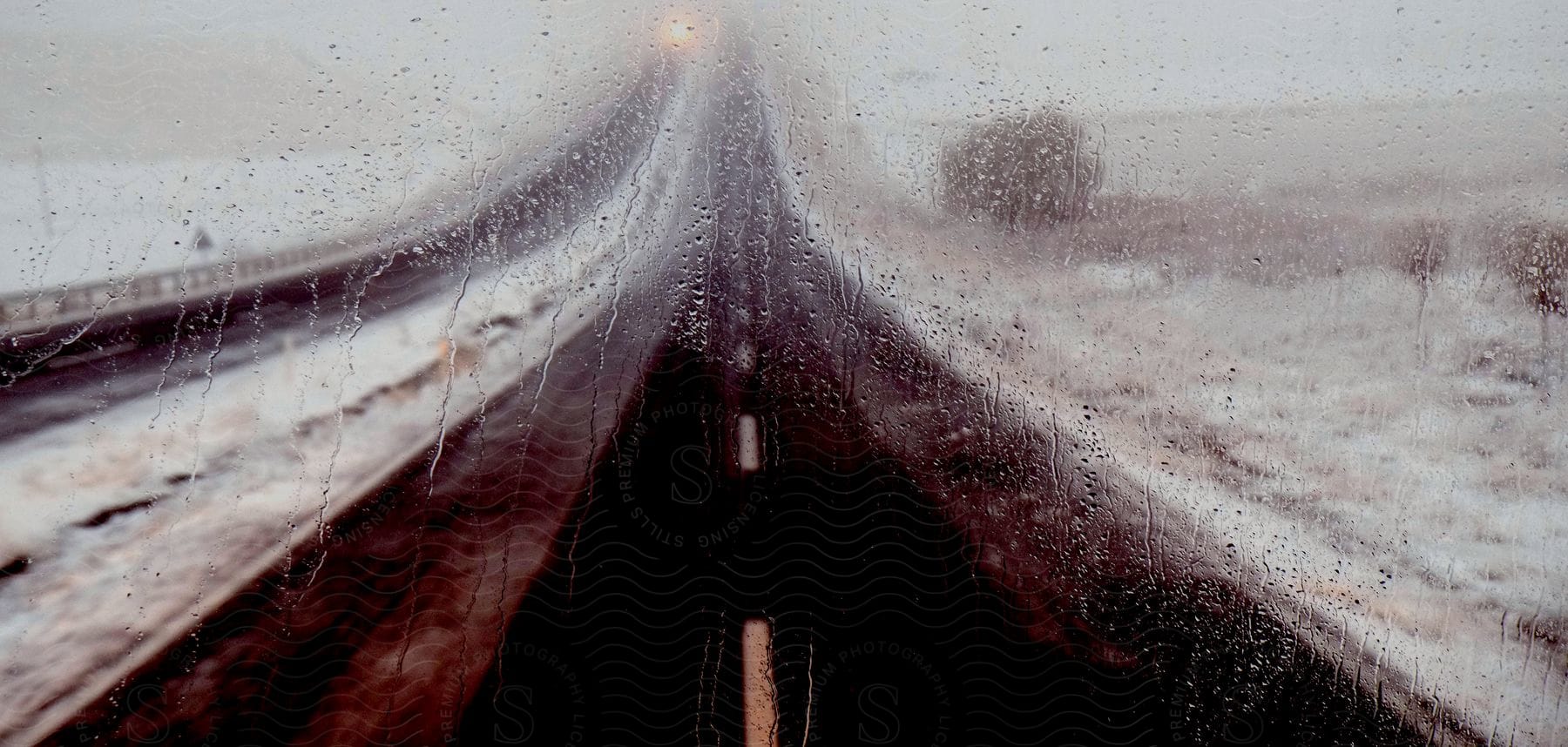 A snowy highway seen through a wet car window at night