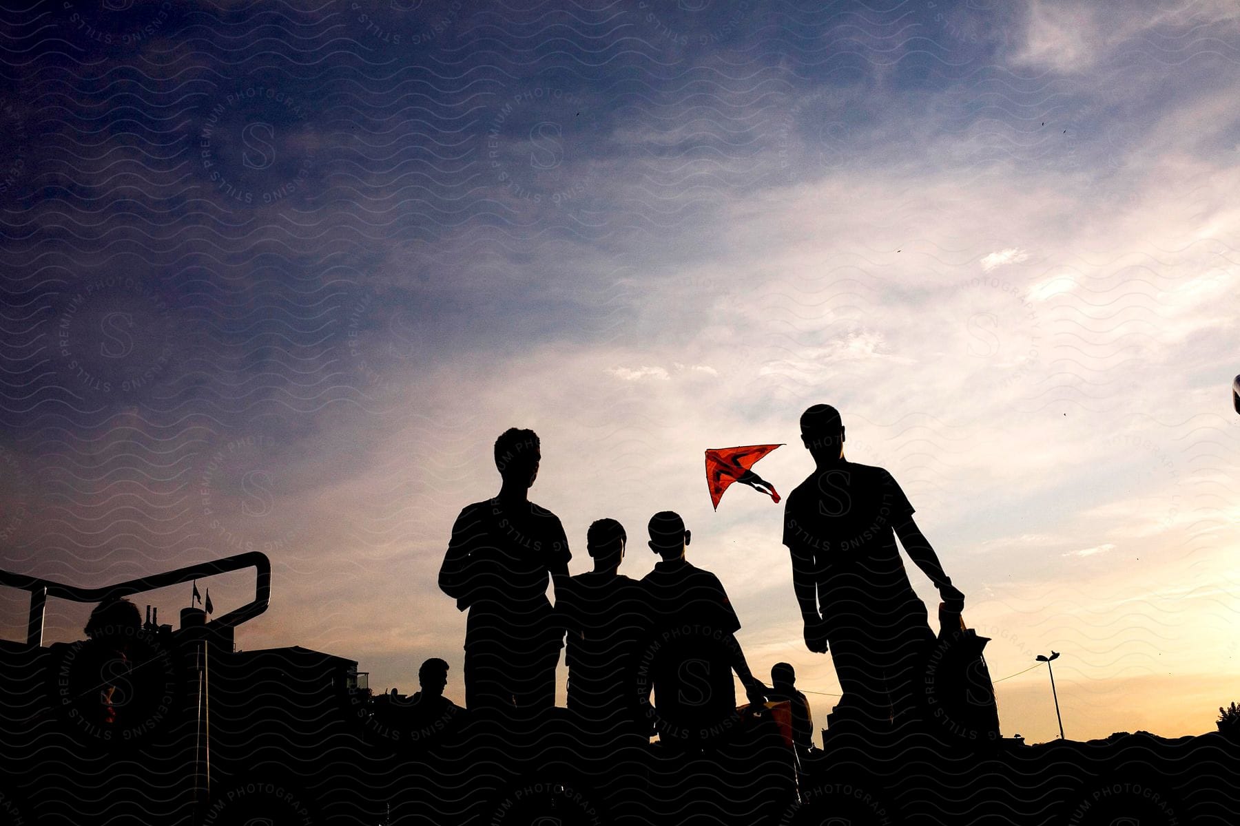 A group of young people flying a spider man kite outdoors at dusk