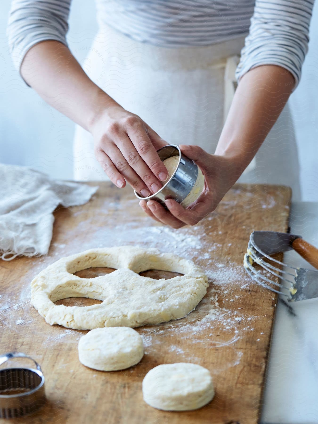 A woman uses a cookie cutter to cut round shapes out of dough on a wooden board