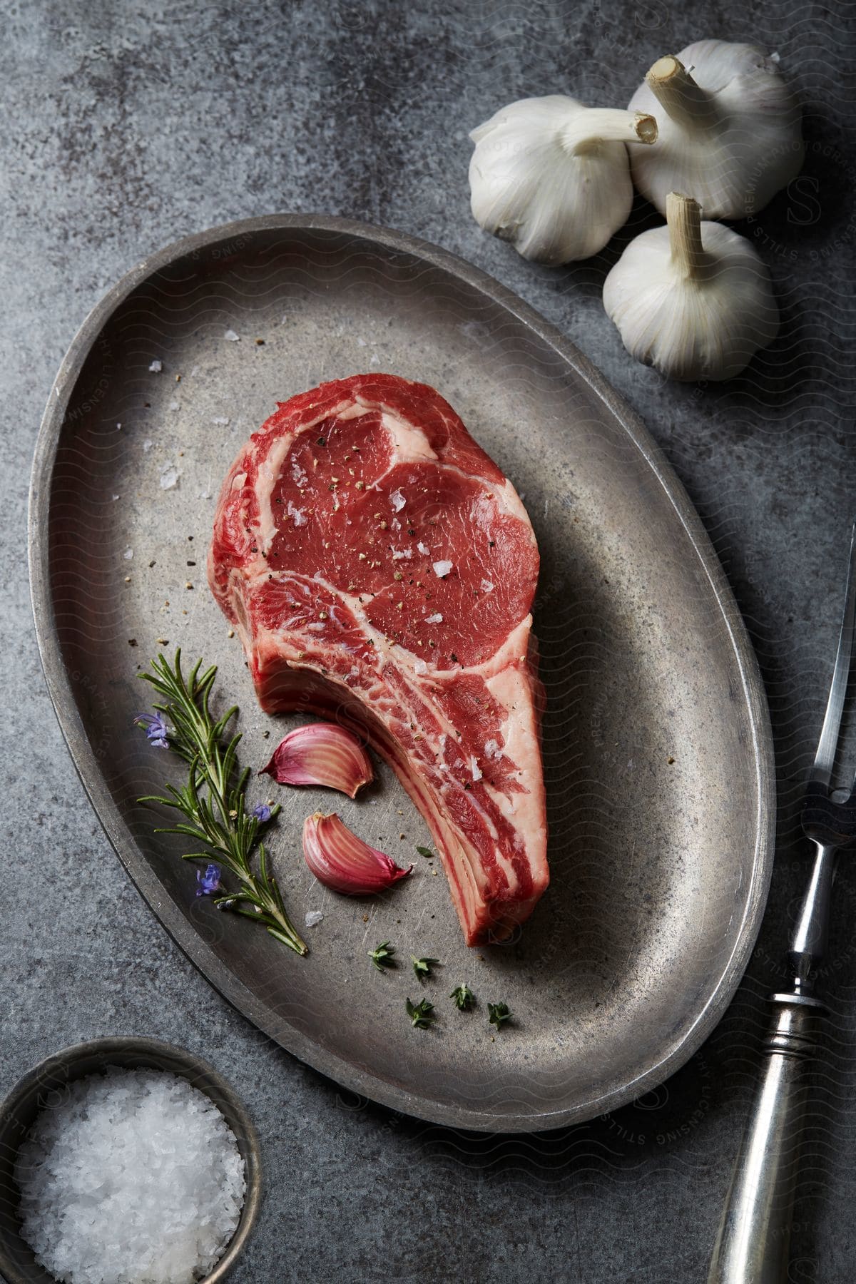 Raw meat is on a plate next to garnish and garlic cloves