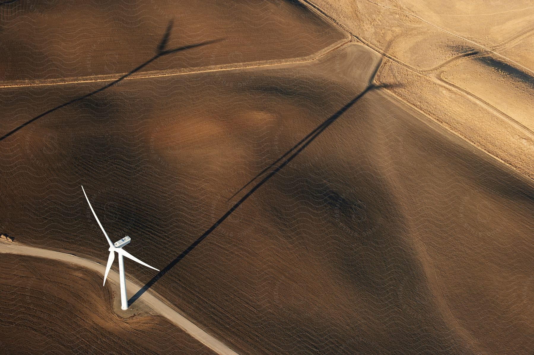 The sun shines on a wind turbine on a wind farm casting shadows on the ground