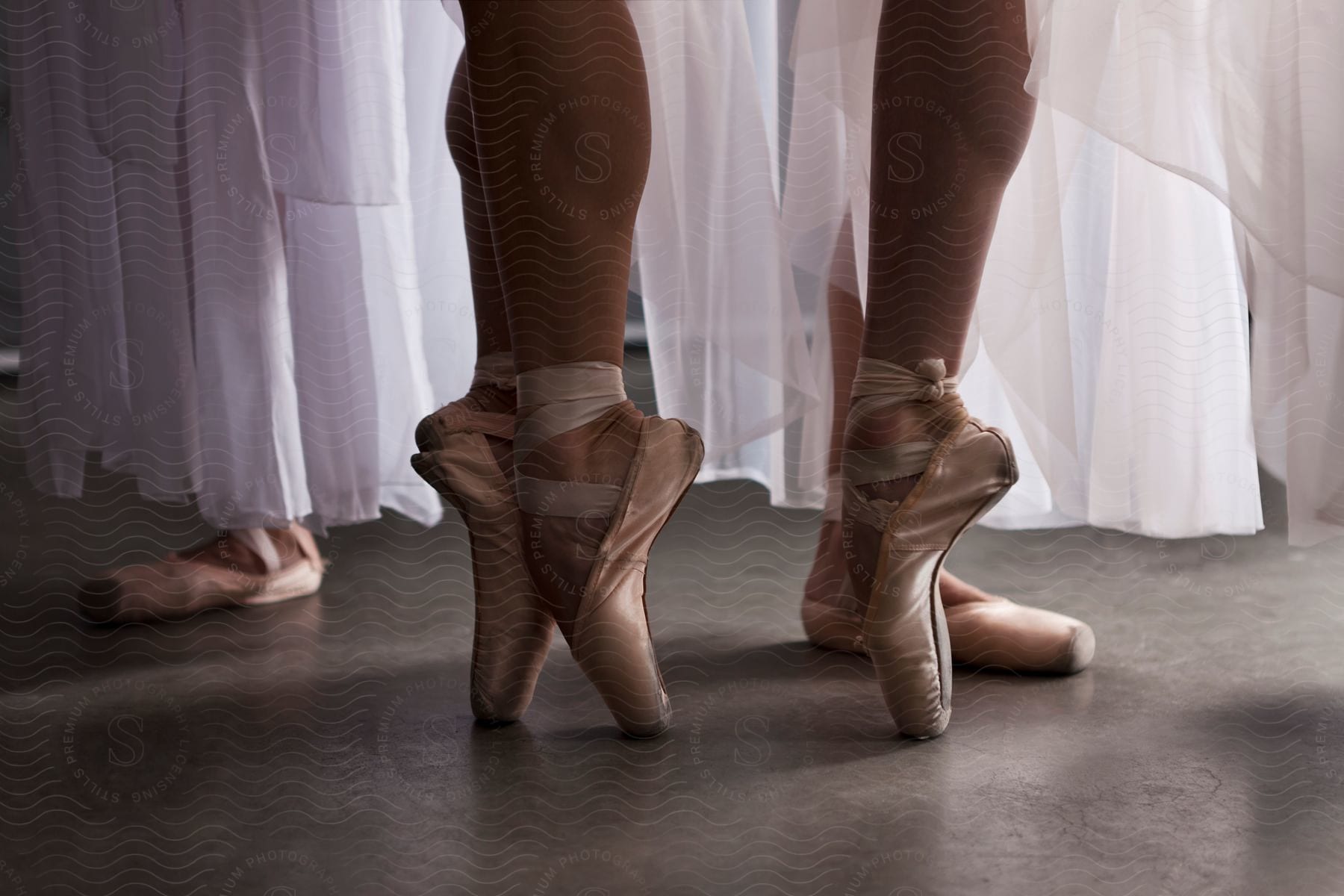 Closeup of pink ballerina shoes on smooth floor with white shirts above them