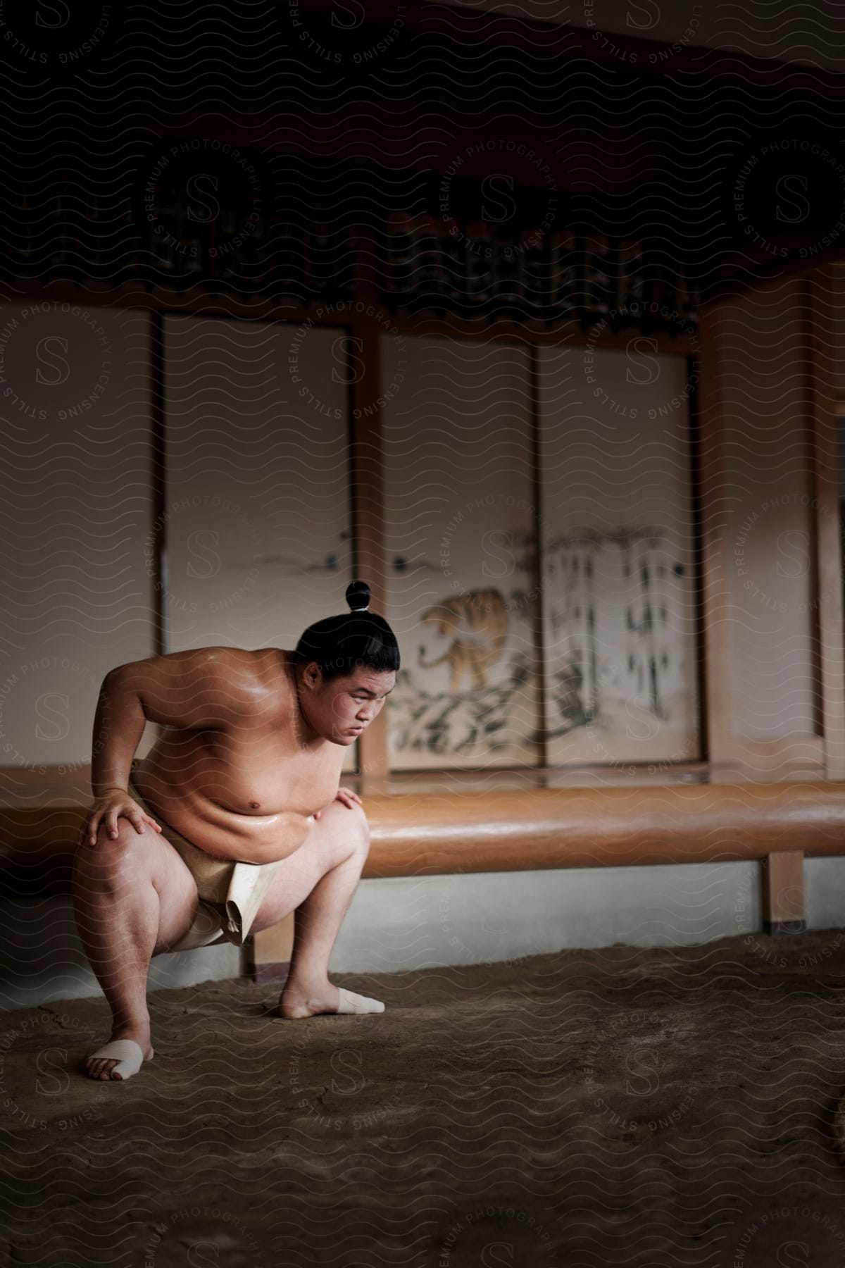 A sumo wrestler crouches down on a dirt floor