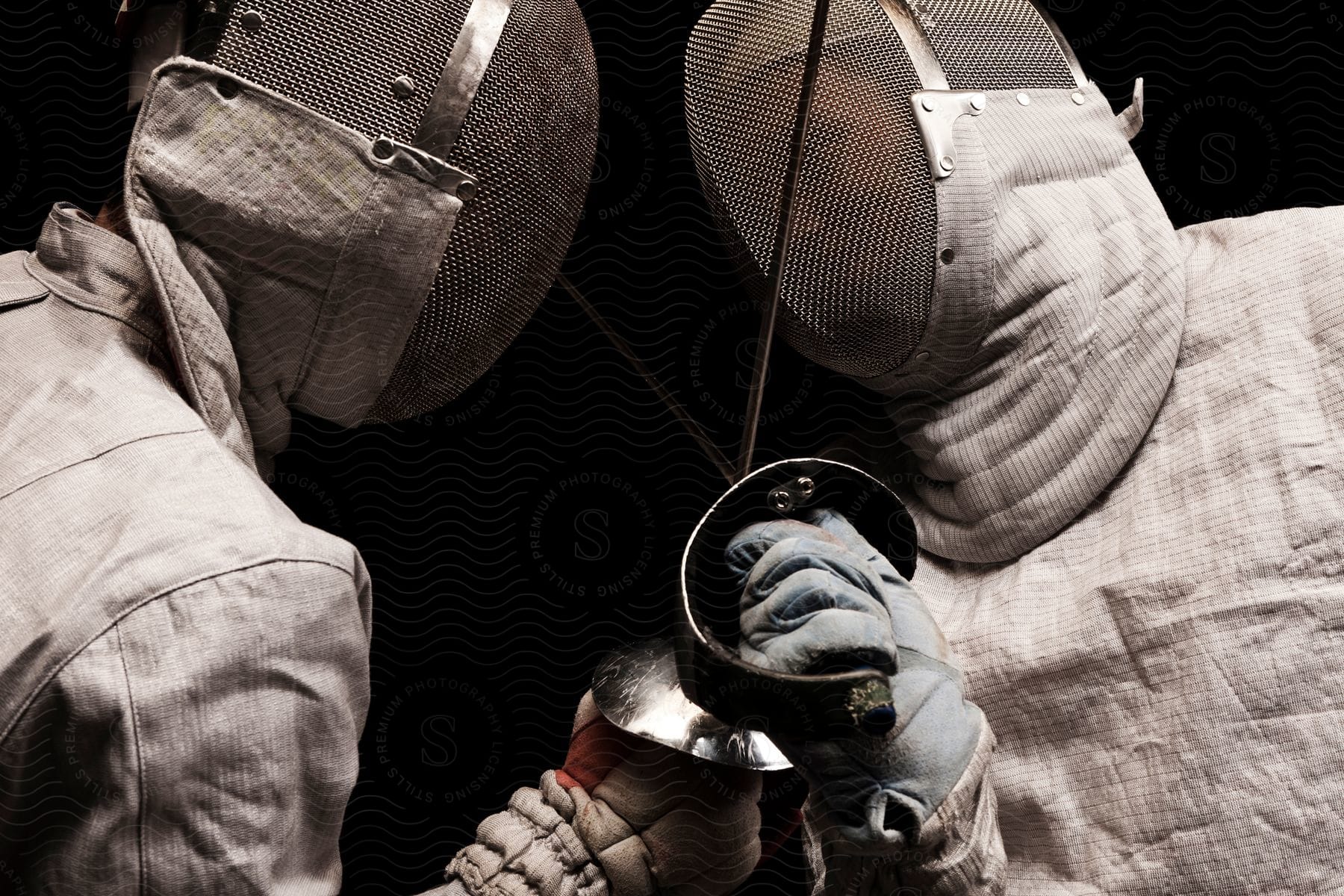 Two individuals engaged in a fencing match wearing masks and fencing attire