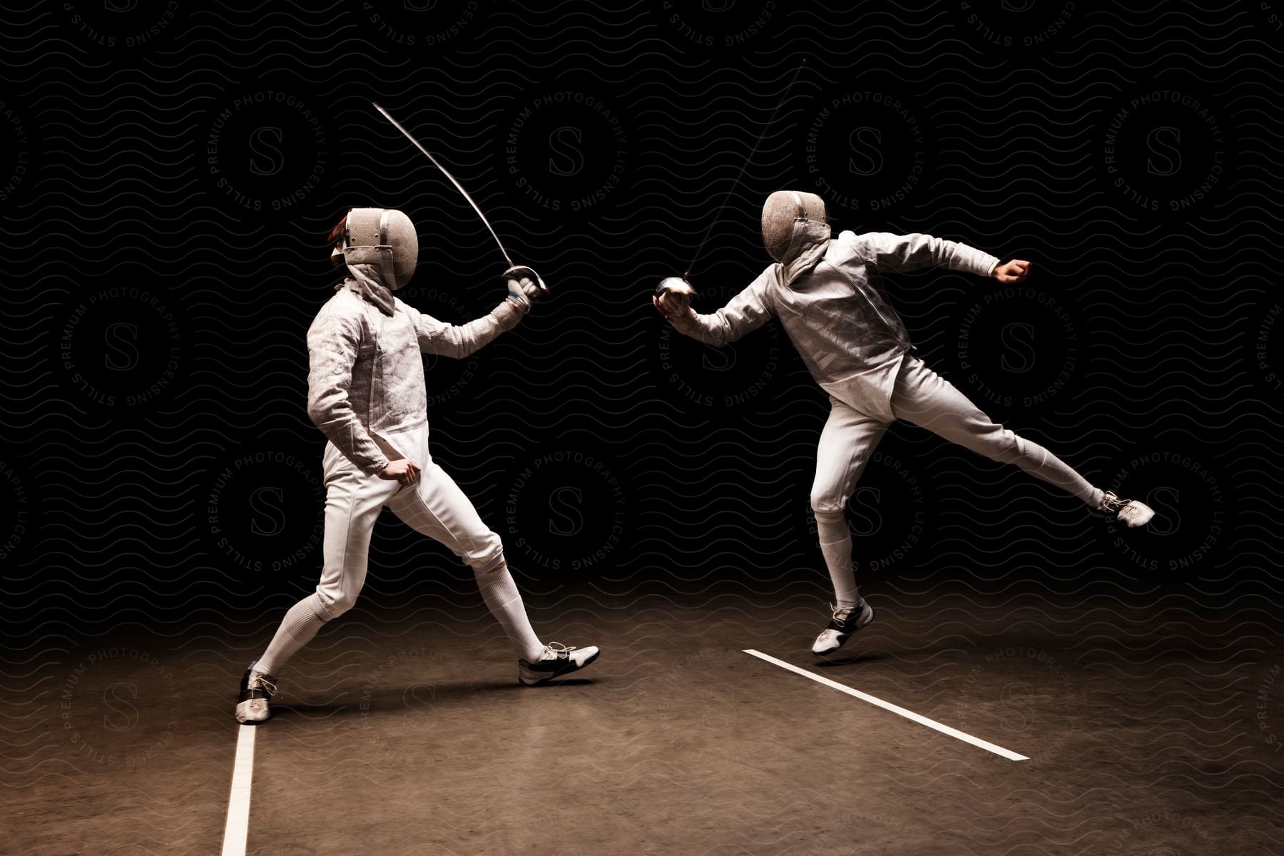 Two fencers practicing in full fencing gear in a dark room with white tape on the glossy floor