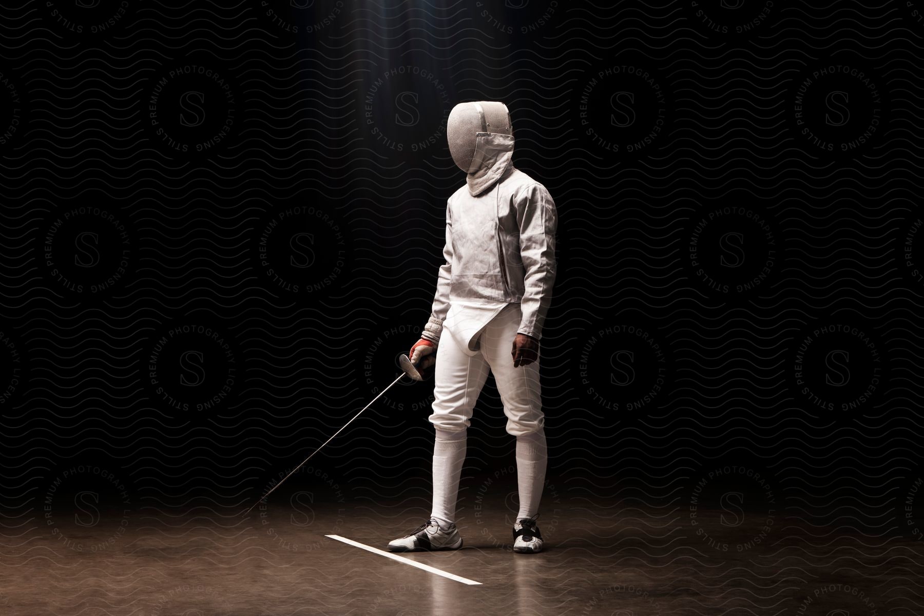 A fencer stands behind a marker on the ground ready to fence