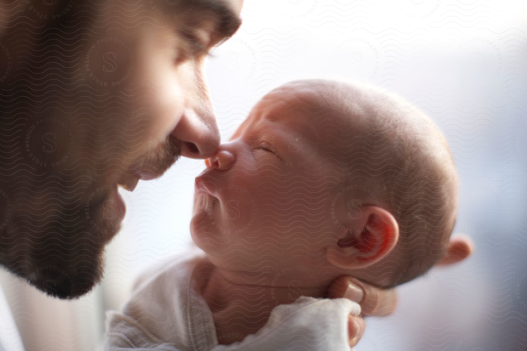 A man holding his newborn baby close nose to nose in a bright room