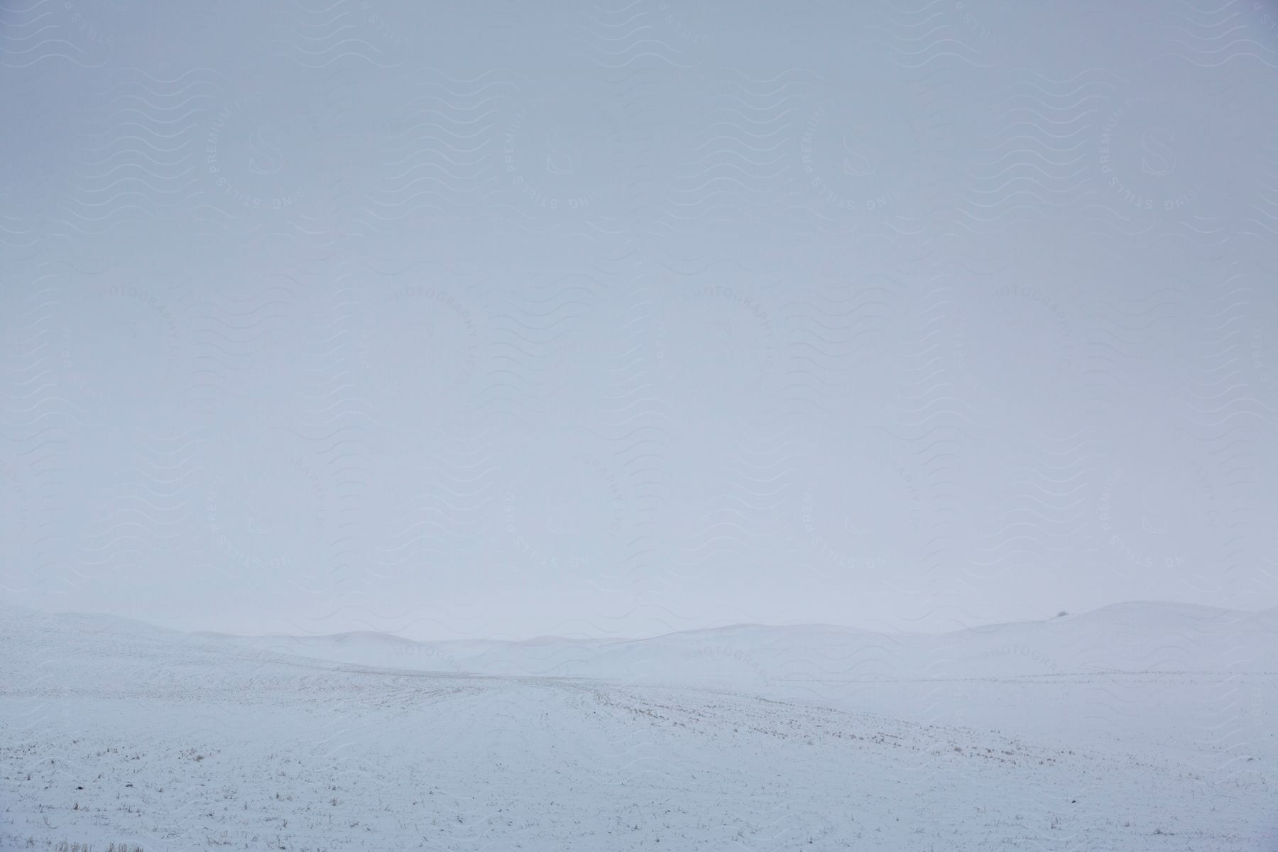 Snow covered ground and mountains in the distance under a hazy white winter sky