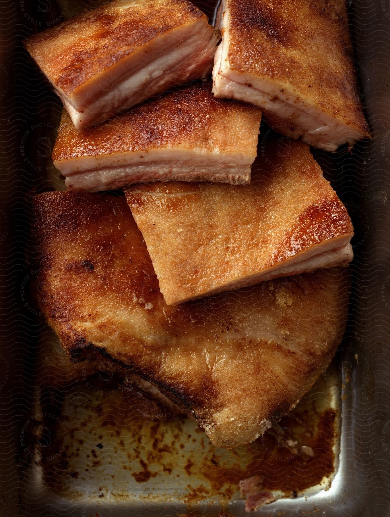 Cut up pieces of pork belly in an aluminum pan with a brown glaze at the bottom