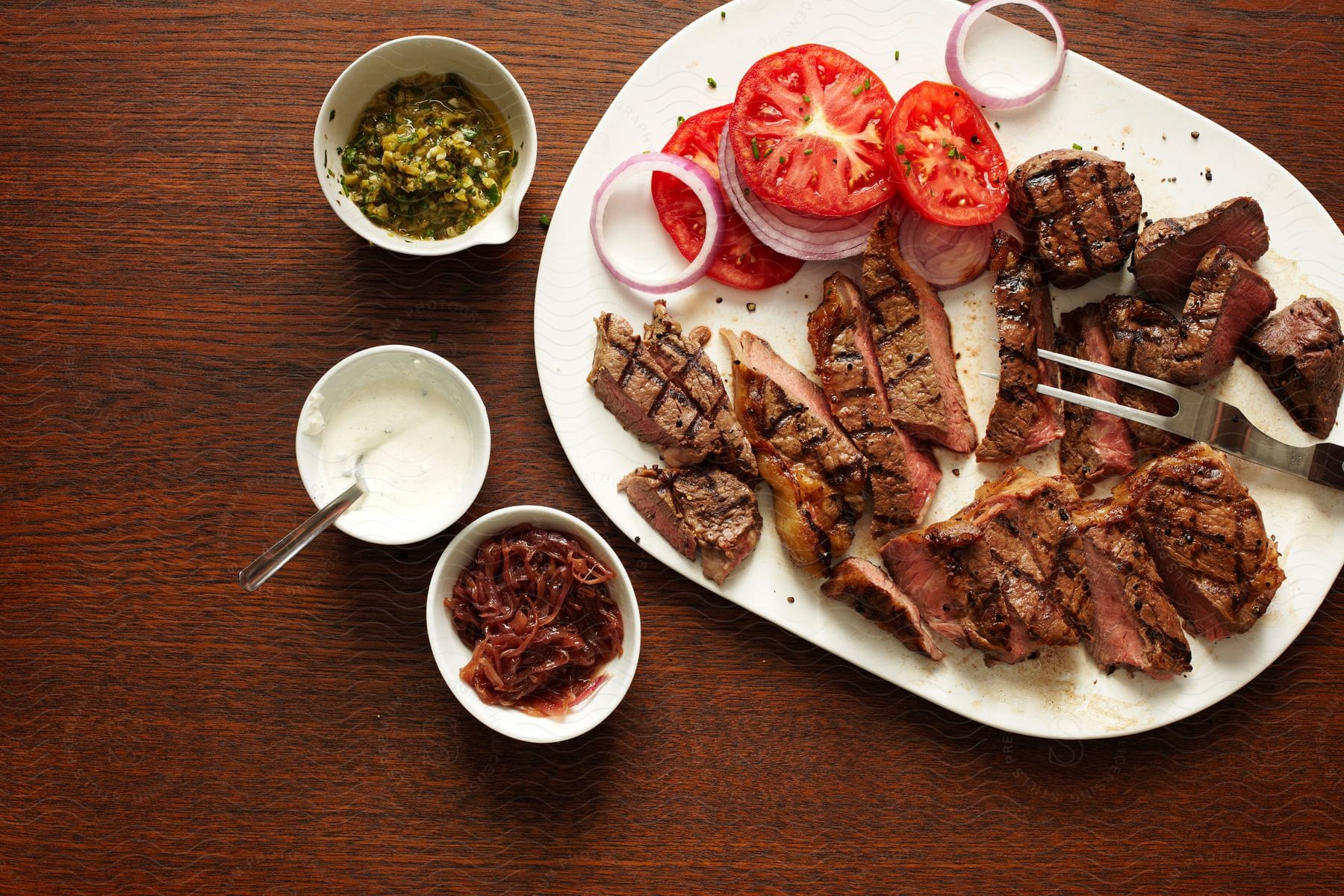 Plate with pieces of meat and tomatoes accompanied by bowls of sauce on a wooden table