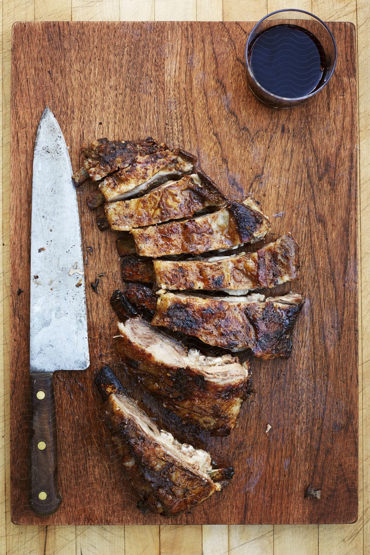 Cooked meat strips on wooden cutting board with knife and glass of wine